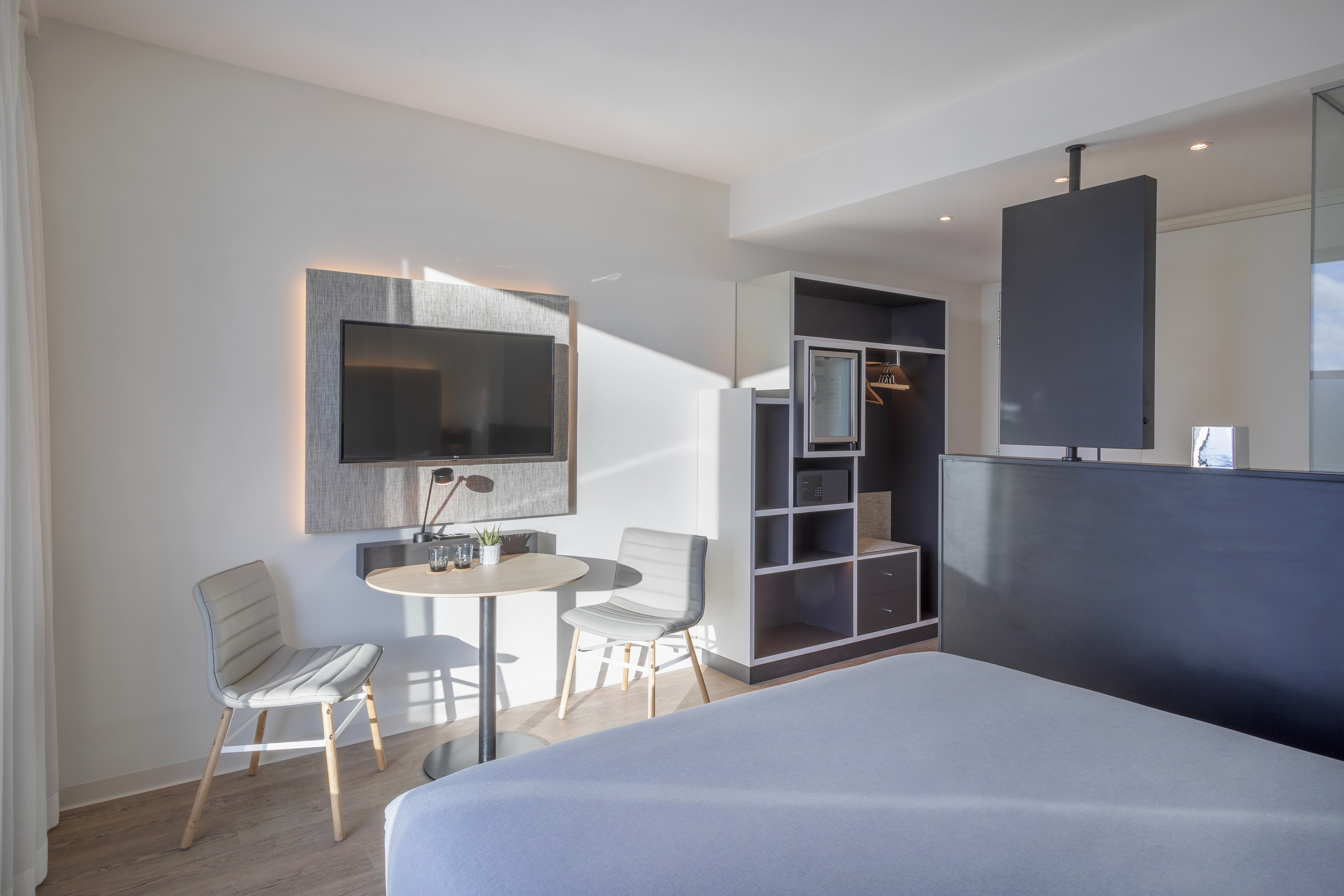 Sleek hotel room with bed, wall TV, small table, chairs, and open closet.