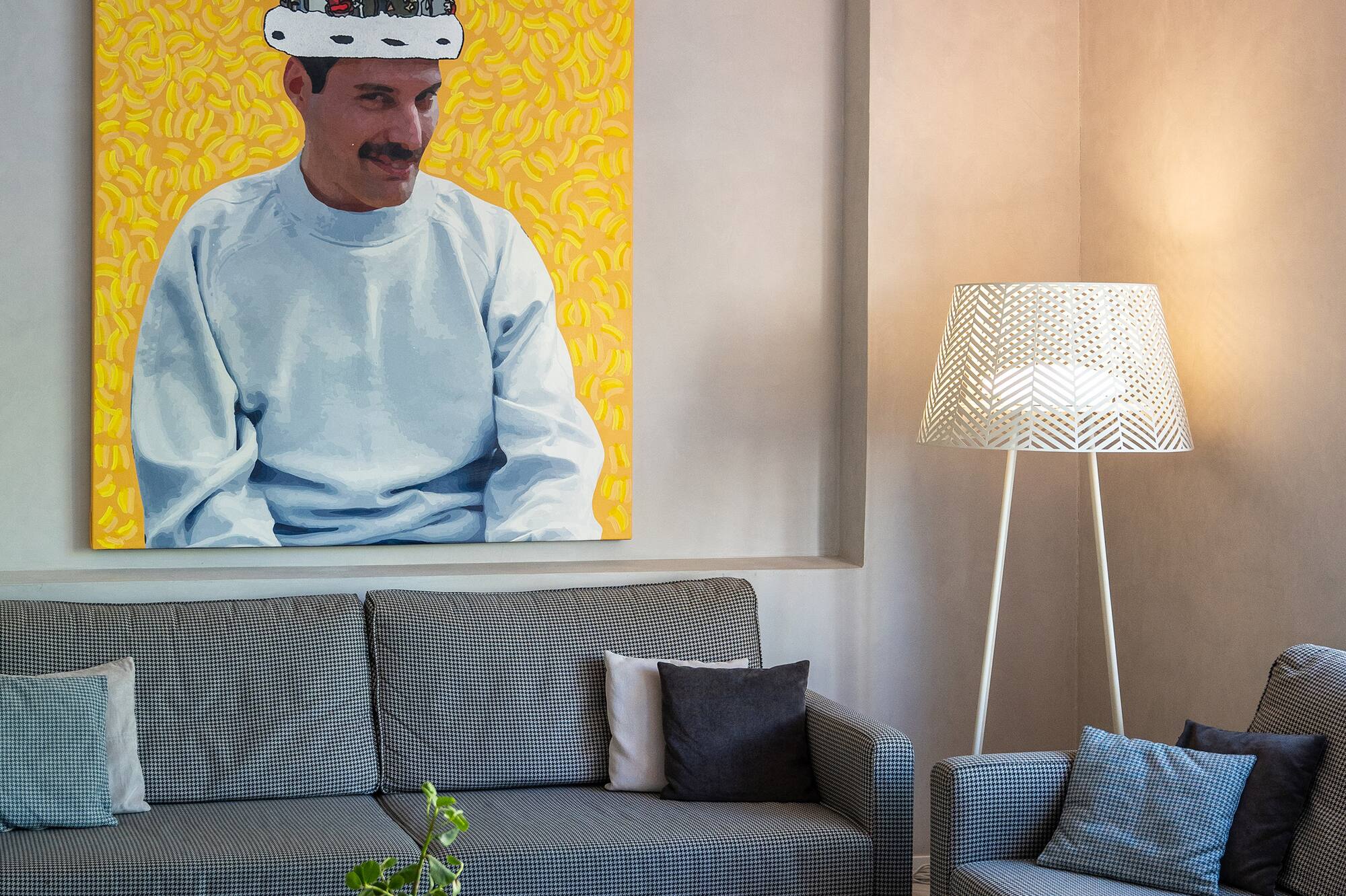 Modern living room with Freddie Mercury art, houndstooth sofas, patterned floor.