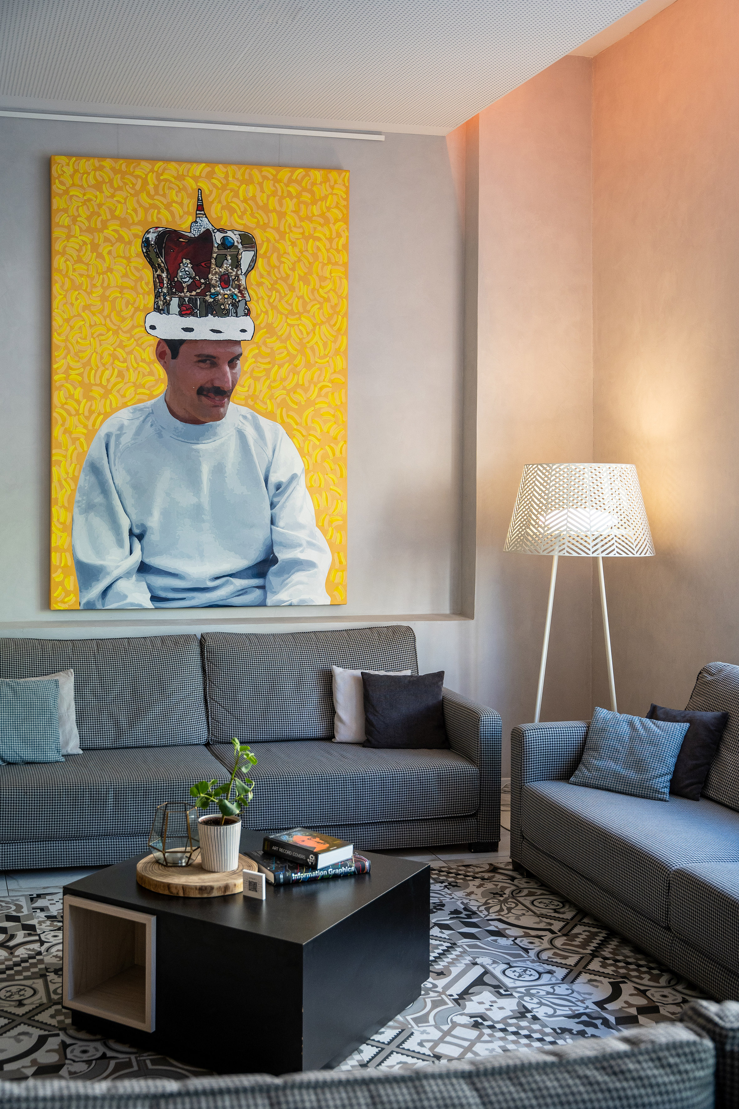 Modern living room with Freddie Mercury art, houndstooth sofas, patterned floor.