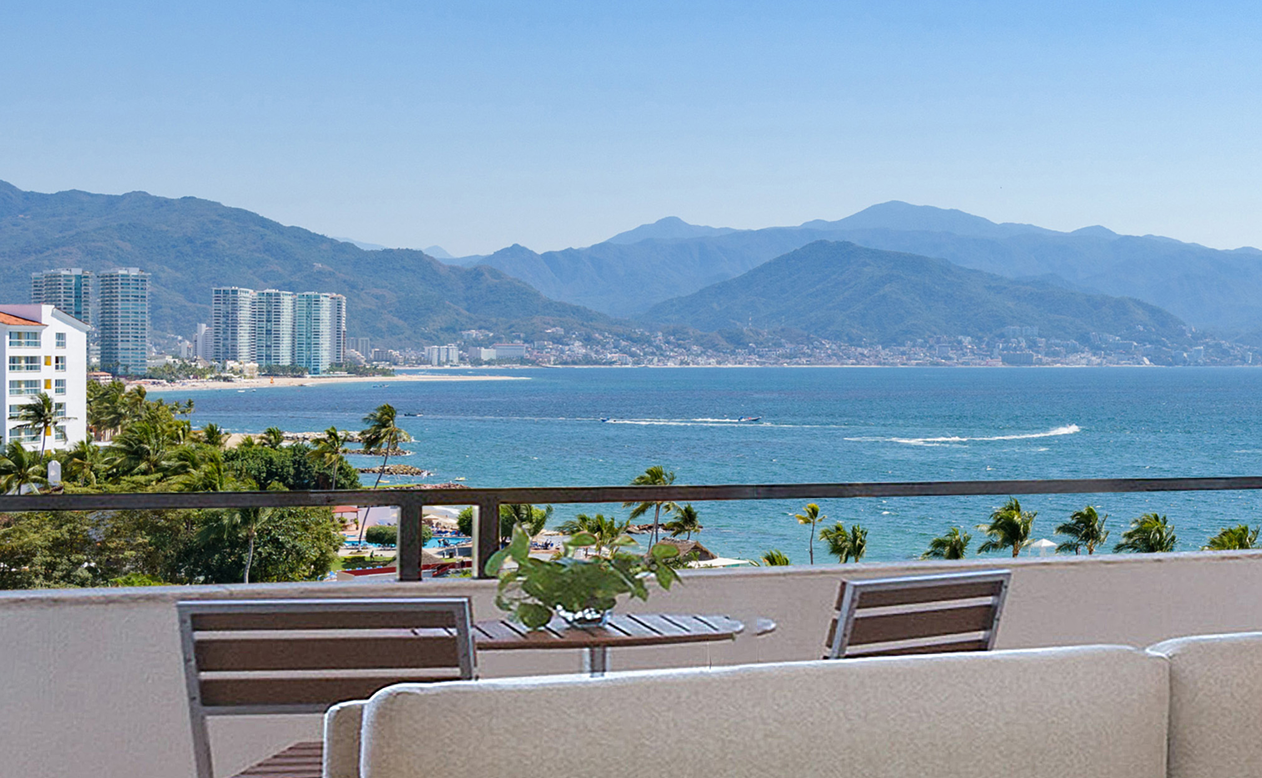 Balcony view: coastal city, expansive bay, mountains, palm trees.