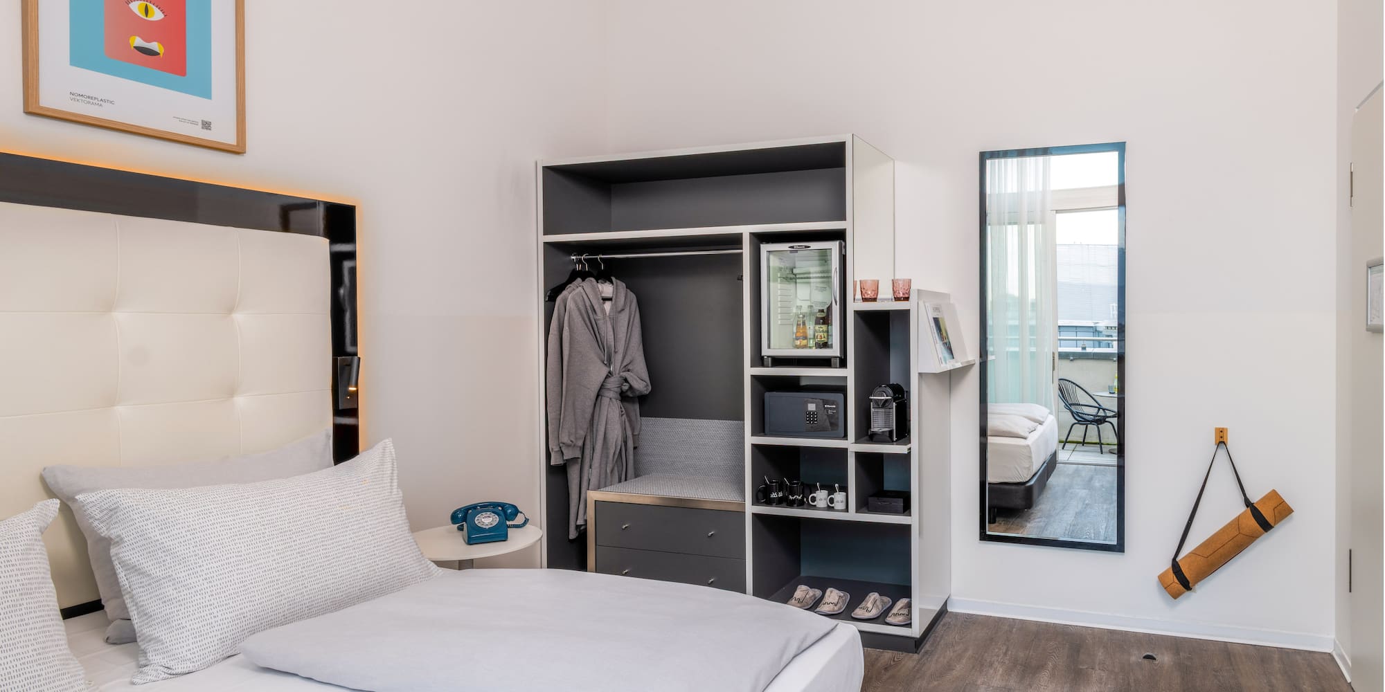 Modern hotel room with bed, integrated wardrobe, minibar, and balcony access.