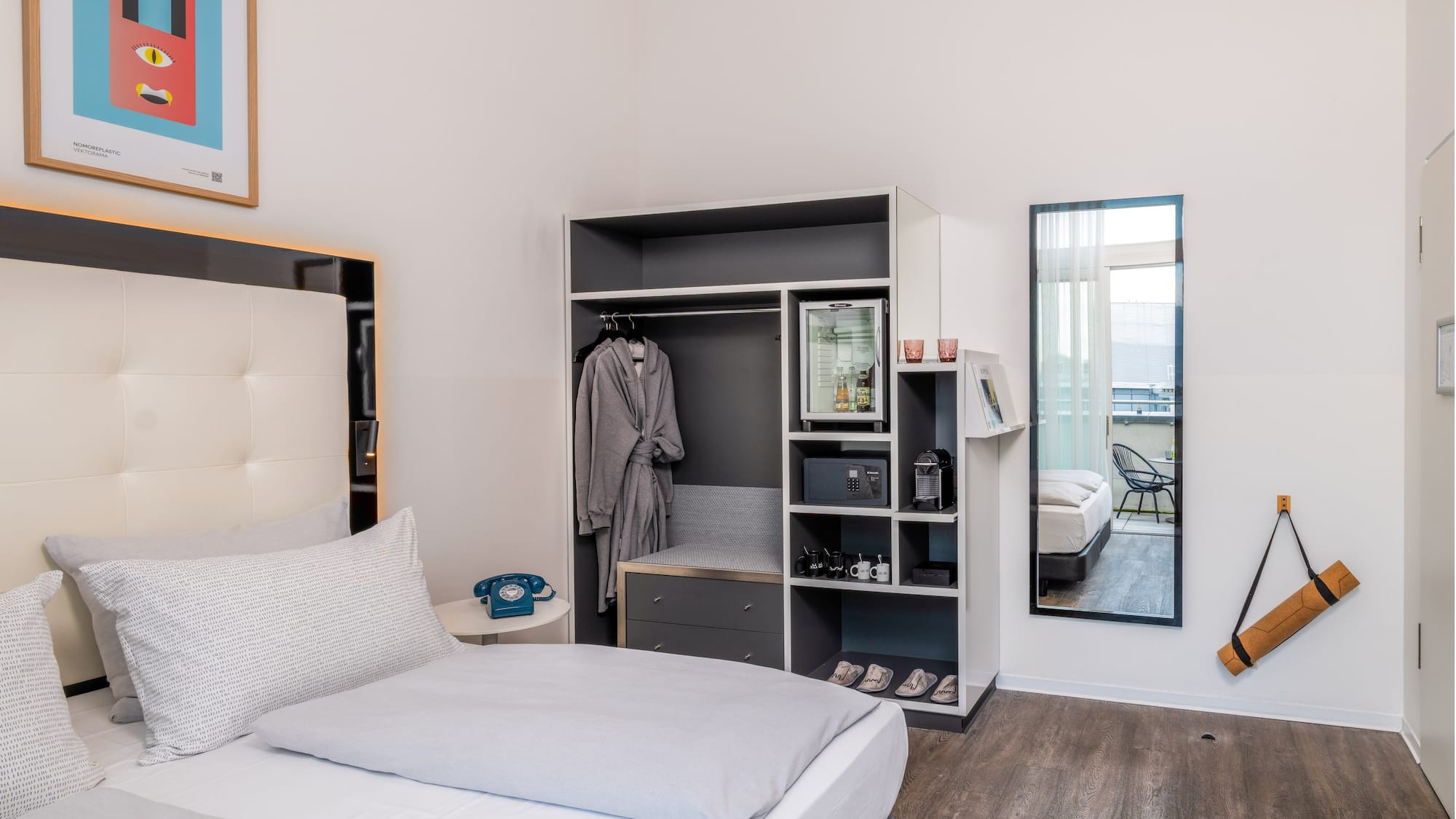 Modern hotel room with bed, integrated wardrobe, minibar, and balcony access.