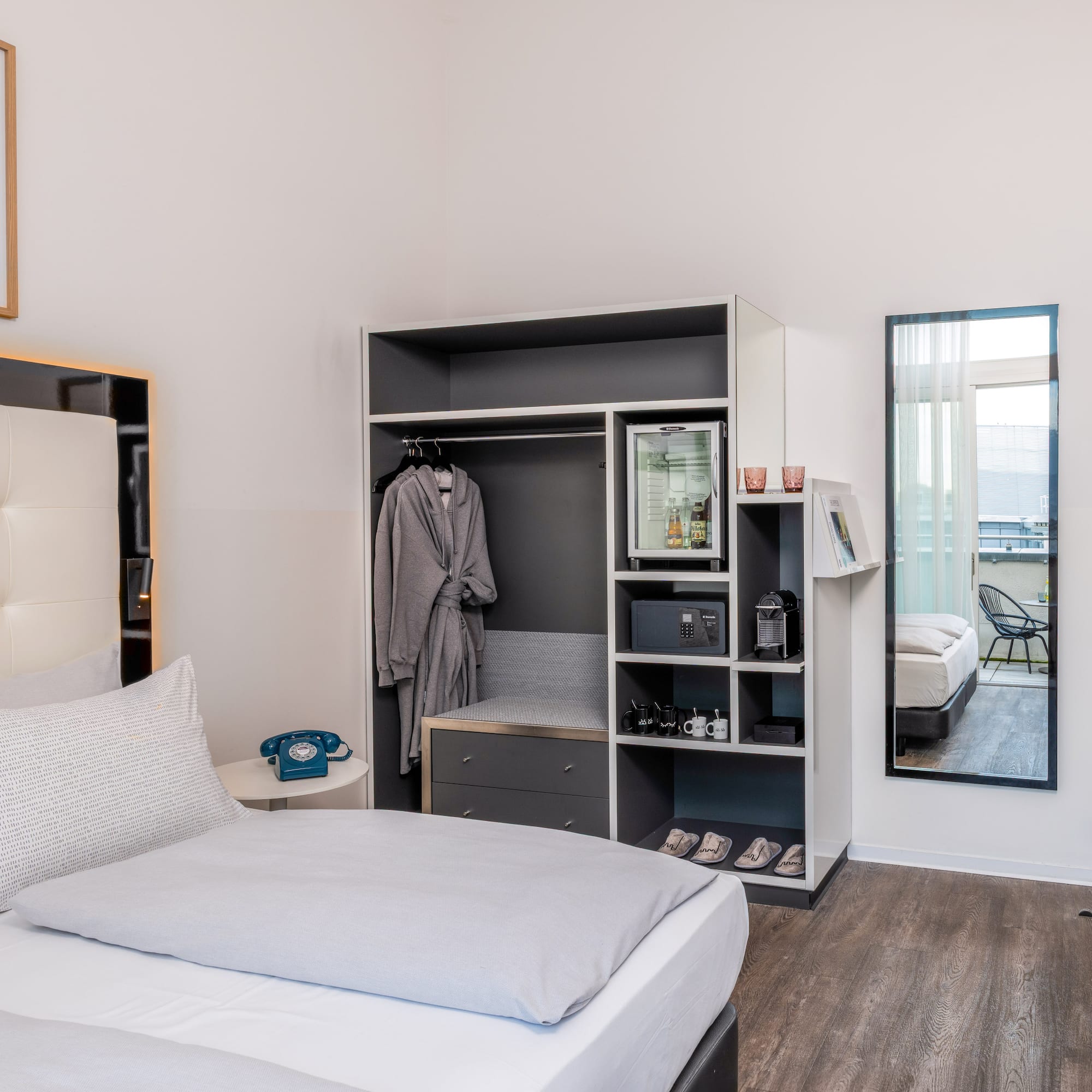 Modern hotel room with bed, integrated wardrobe, minibar, and balcony access.