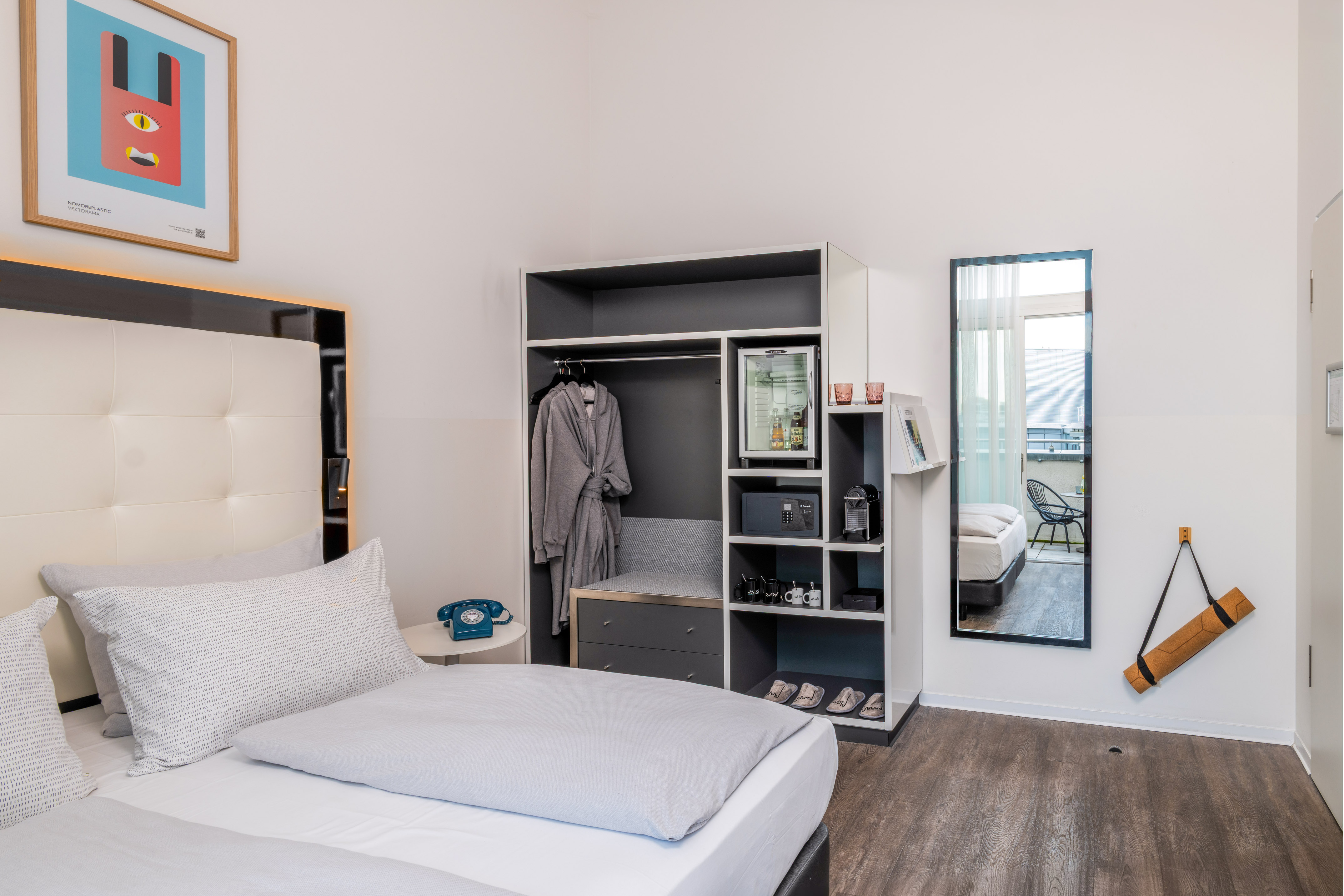 Modern hotel room with bed, integrated wardrobe, minibar, and balcony access.