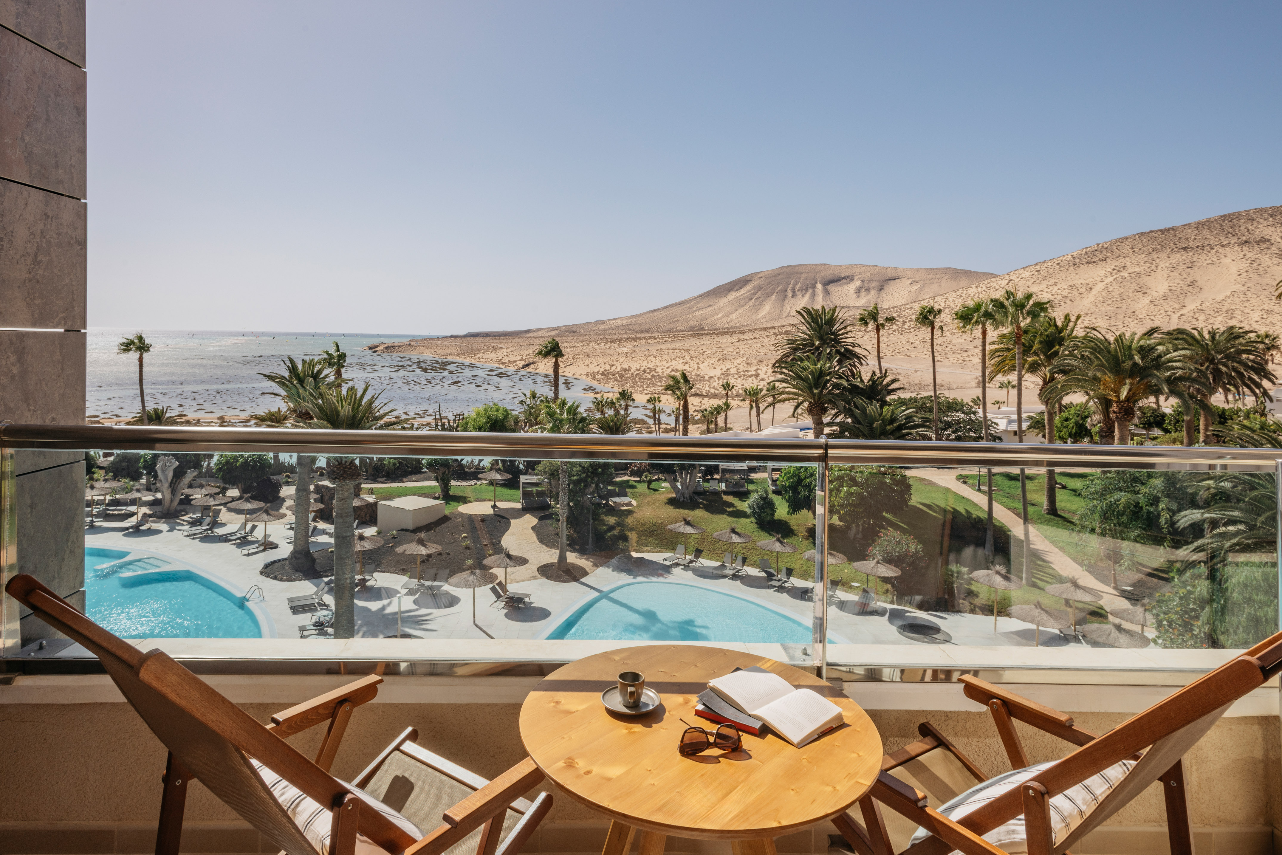 Balcony view of ocean, resort pools, palm trees, and desert hills.