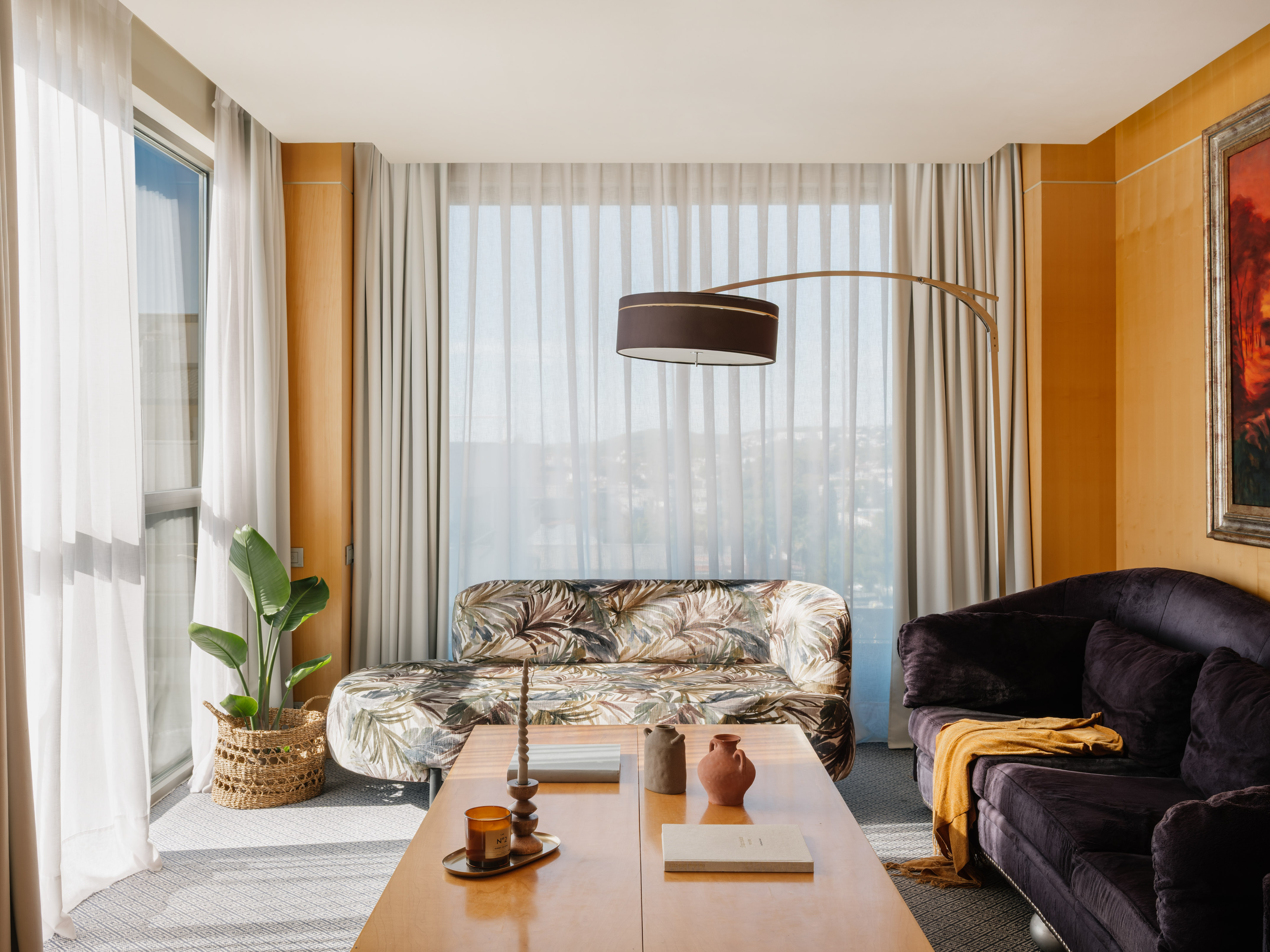 Bright living room with patterned sofa, dark sofa, coffee table, and sheer window.