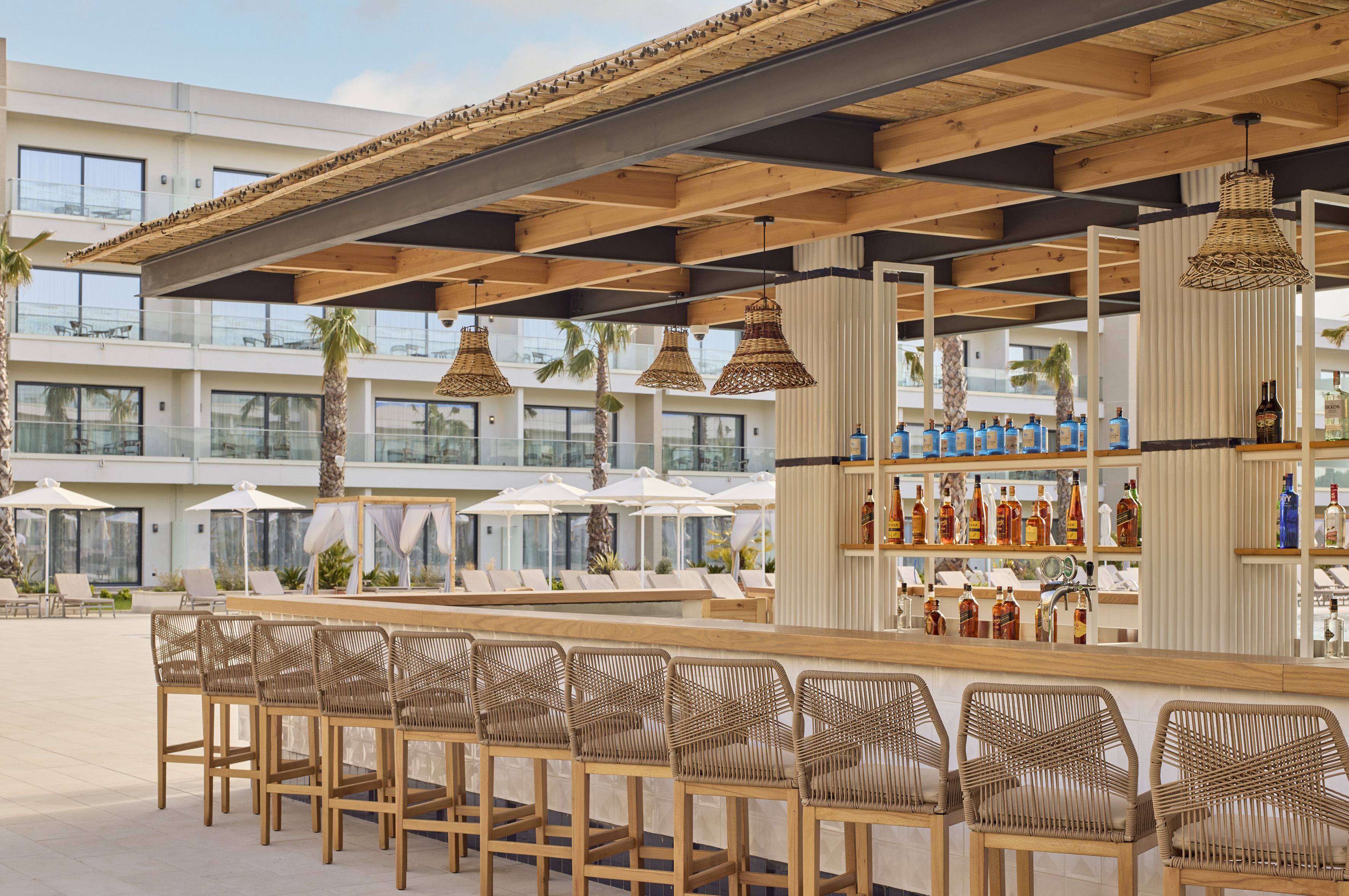Outdoor resort bar with thatched roof, wicker stools, and bottled spirits.
