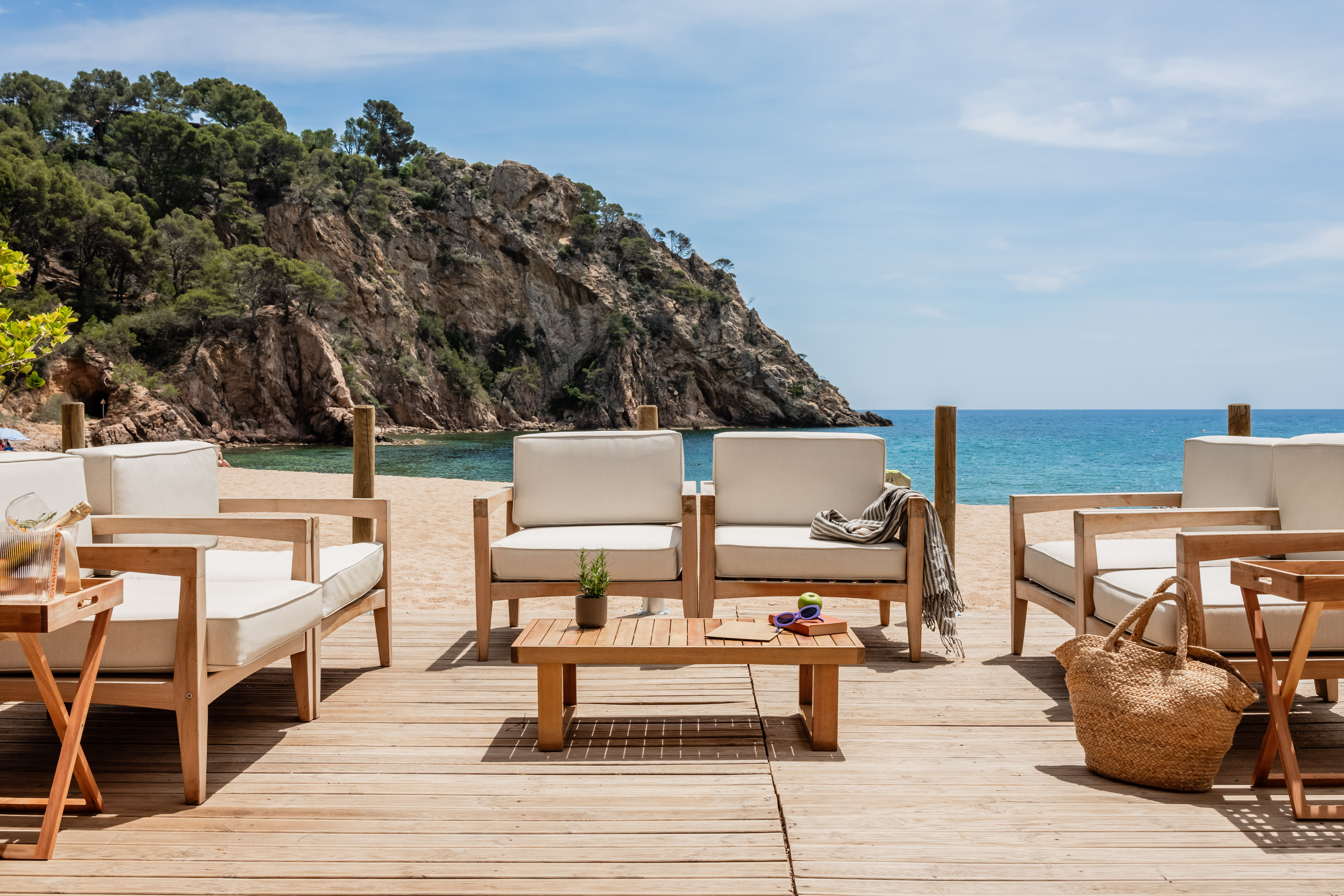 Coastal outdoor teak lounge furniture on wooden deck with ocean and cliff view.
