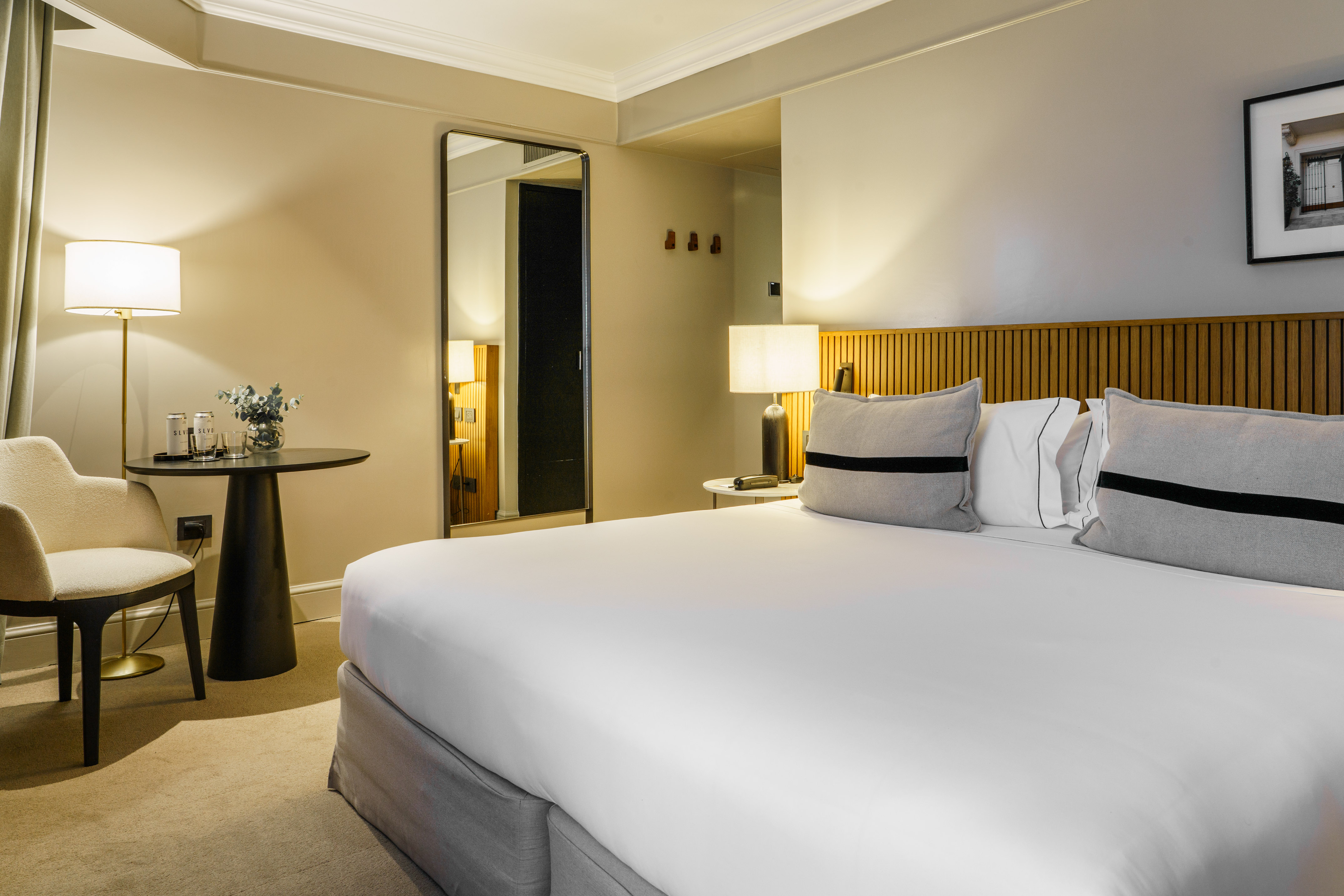 Modern hotel bedroom with large bed, wooden headboard, and elegant side seating.