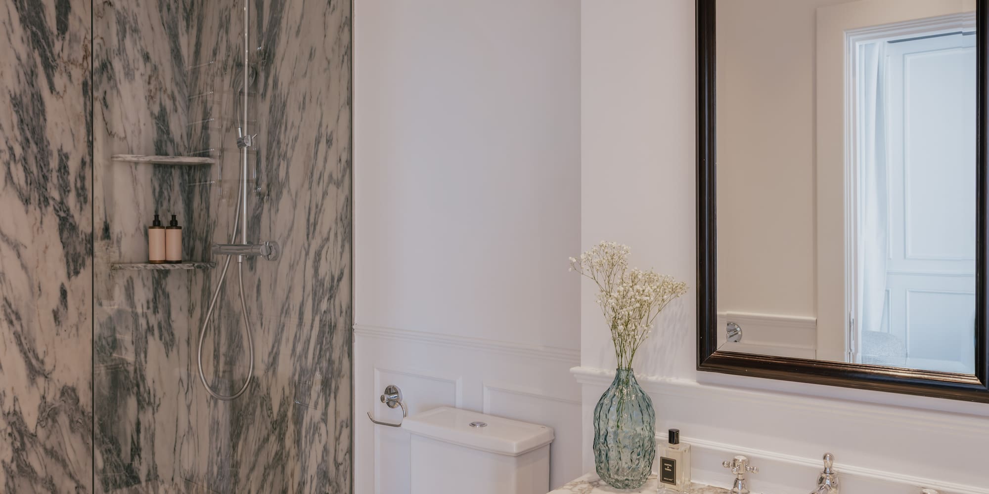 Luxury bathroom interior: marble walk-in shower, white vanity, and elegant mirror.