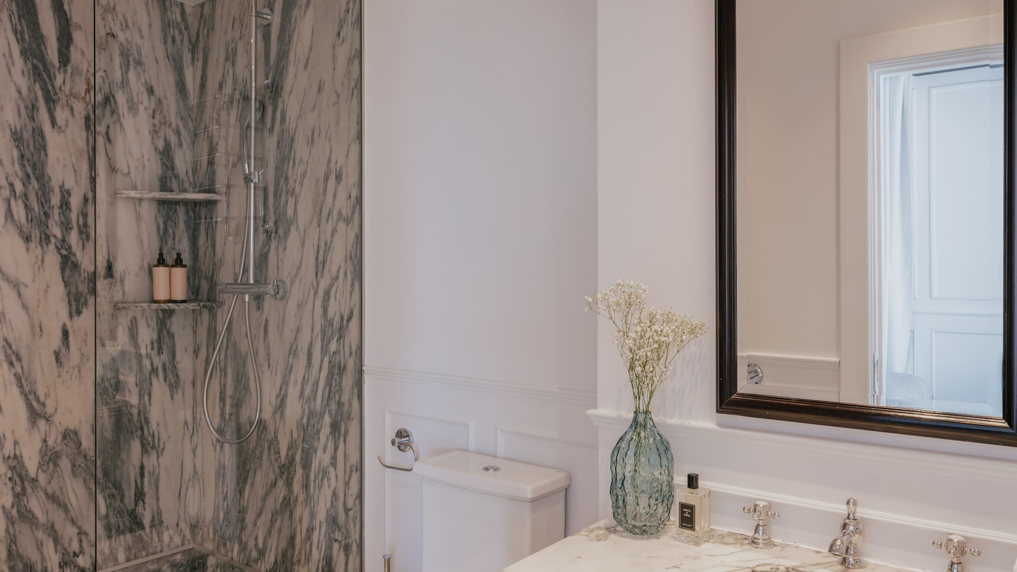Elegant bathroom with marble shower, white vanity, toilet, and large mirror.