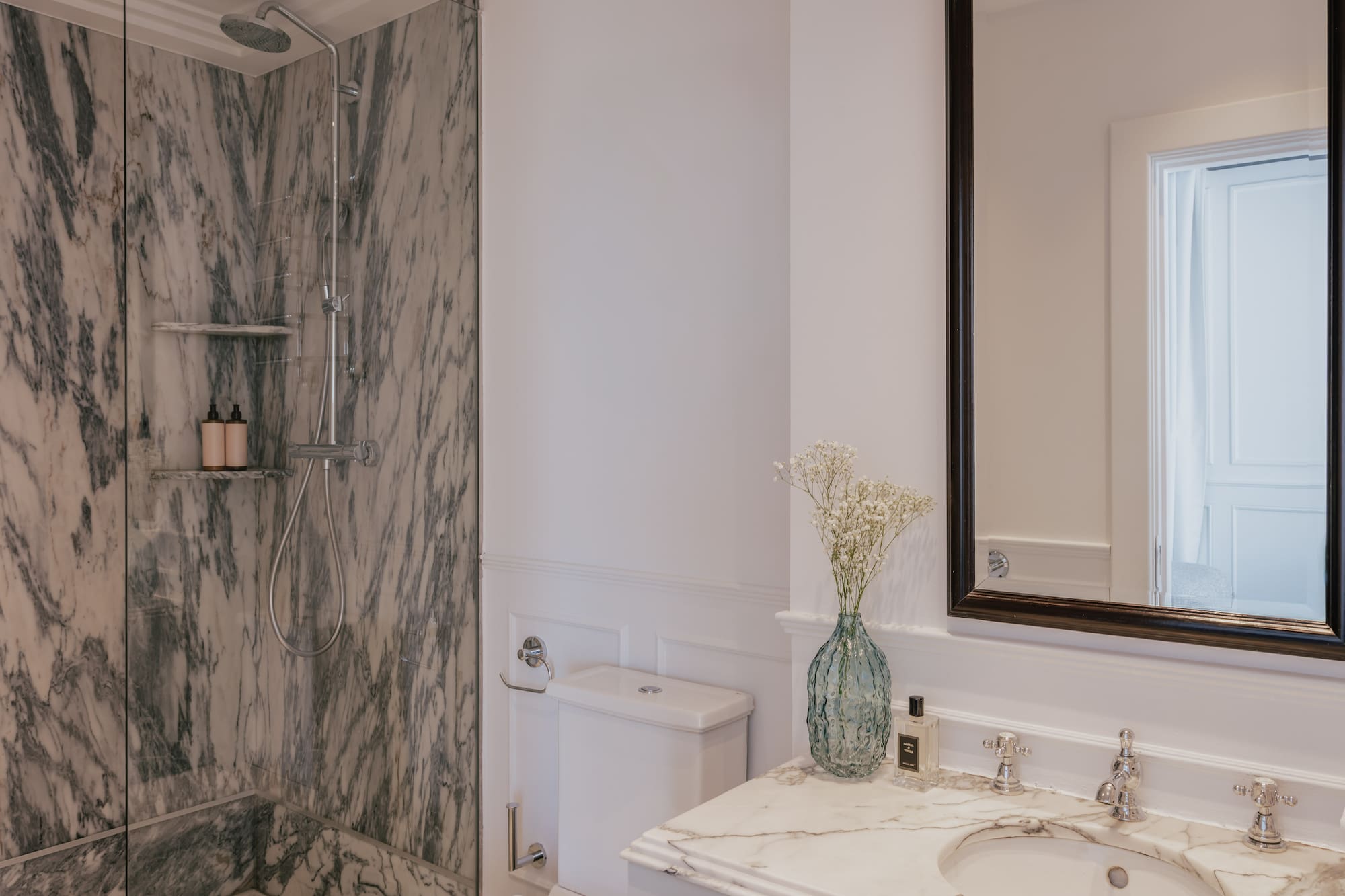 Luxury bathroom interior: marble walk-in shower, white vanity, and elegant mirror.