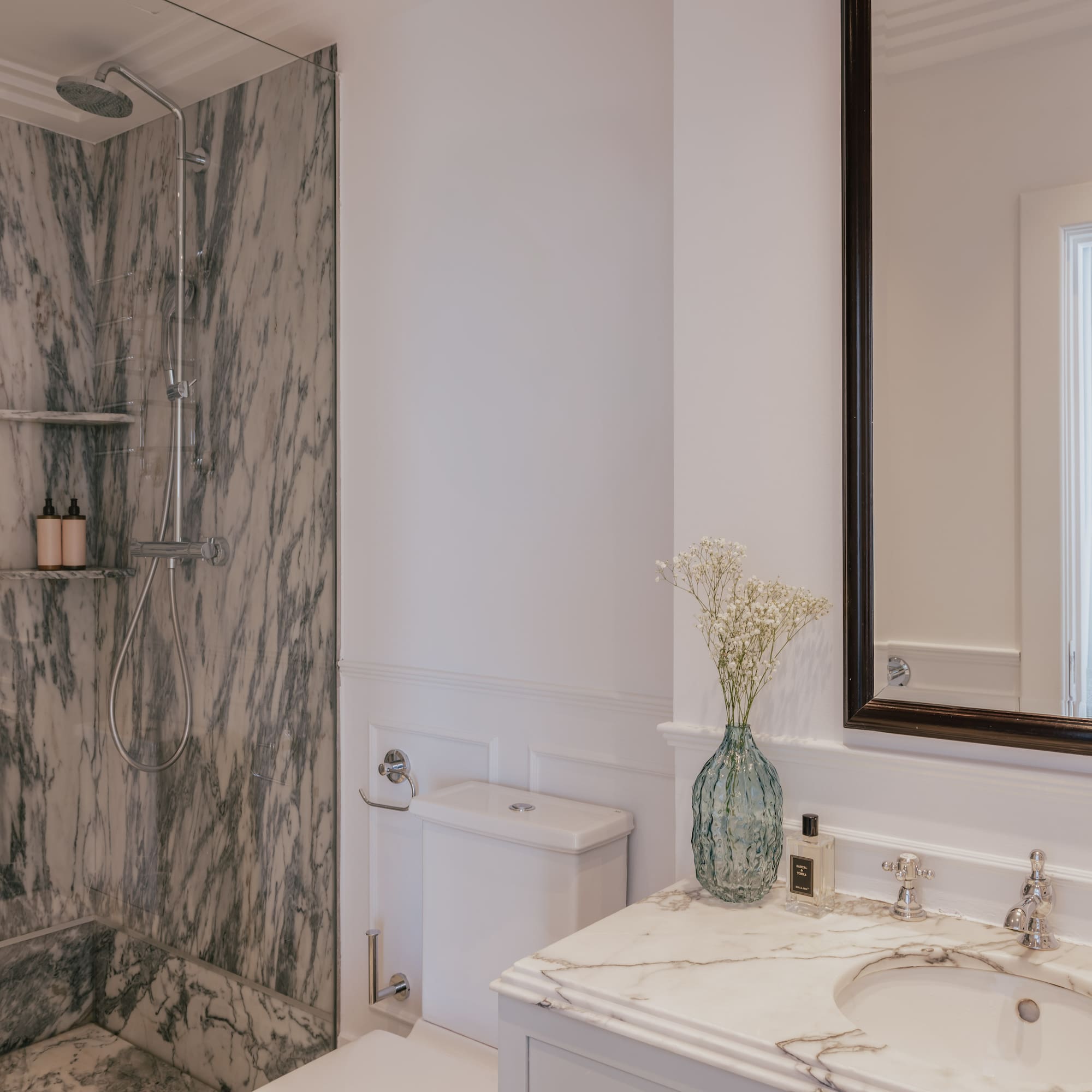 Luxury bathroom interior: marble walk-in shower, white vanity, and elegant mirror.