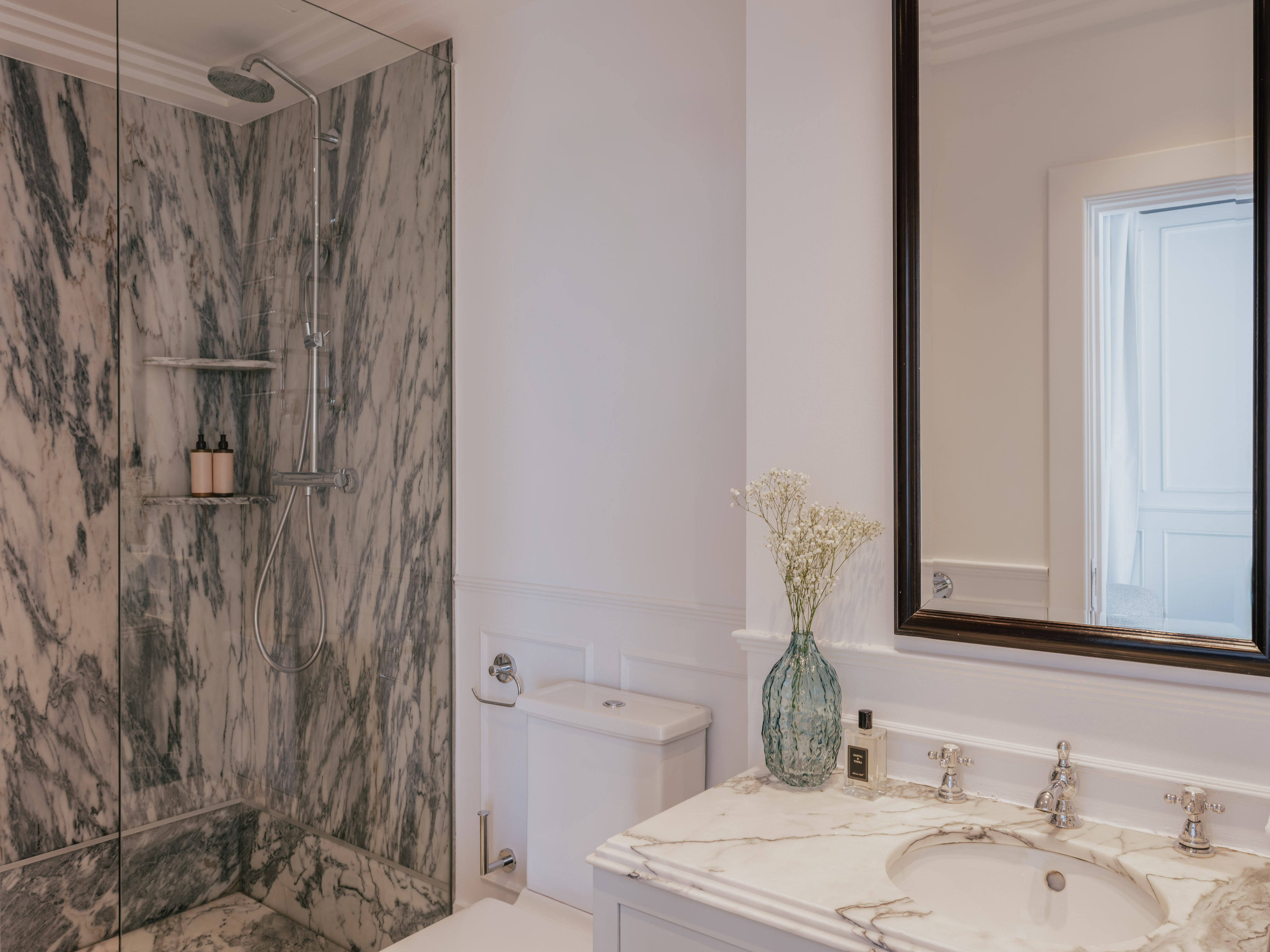 Luxury bathroom interior: marble walk-in shower, white vanity, and elegant mirror.