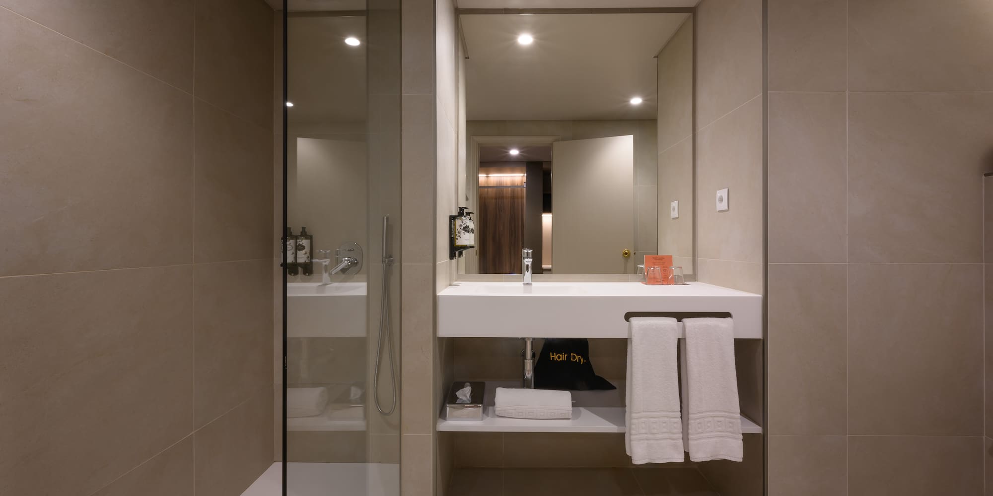 Modern hotel bathroom with walk-in shower, floating vanity, and fresh towels.