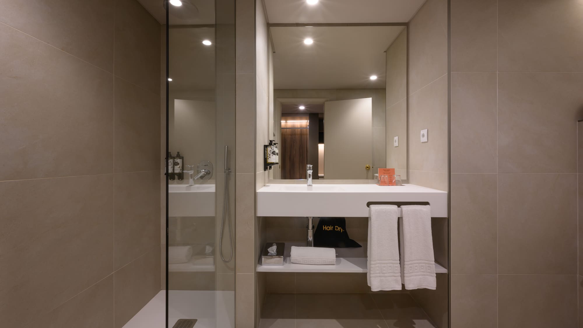 Modern hotel bathroom with walk-in shower, floating vanity, and fresh towels.