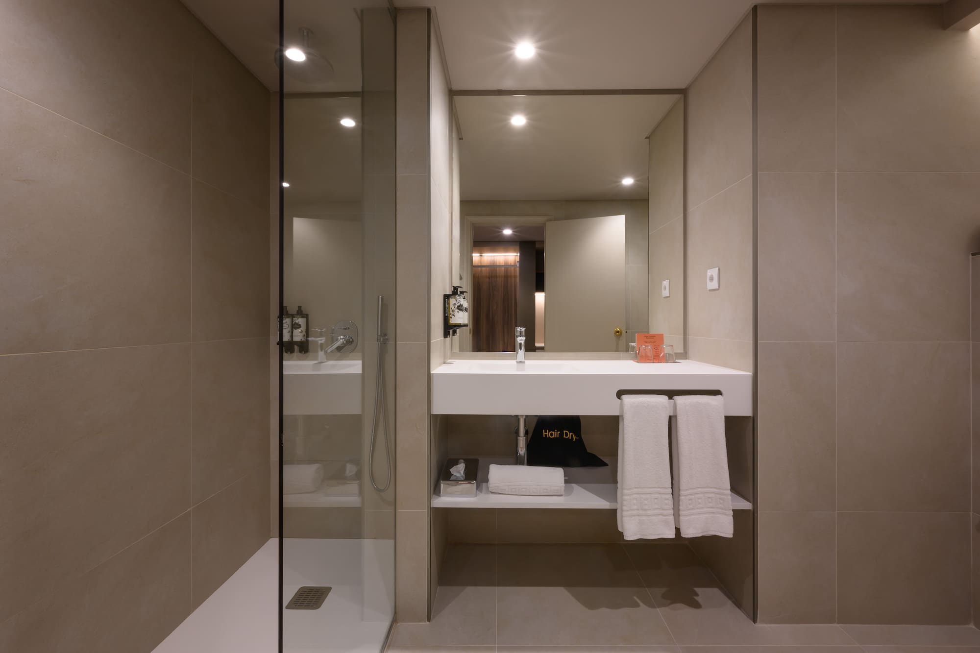 Modern hotel bathroom with walk-in shower, floating vanity, and fresh towels.