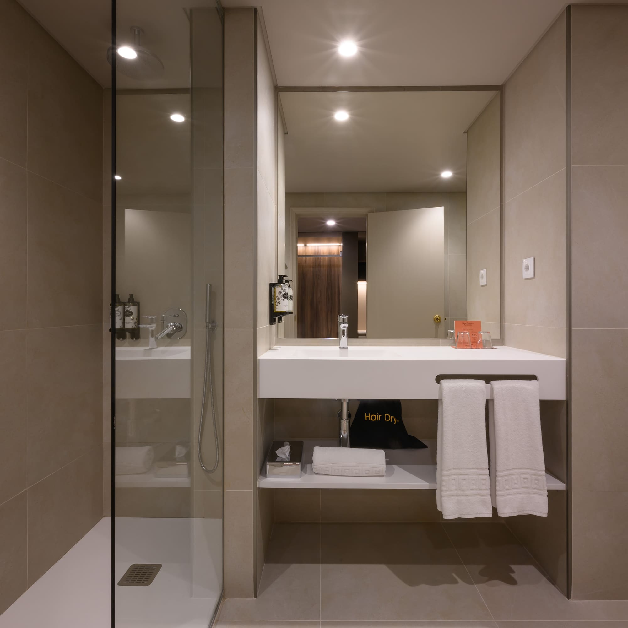 Modern hotel bathroom with walk-in shower, floating vanity, and fresh towels.