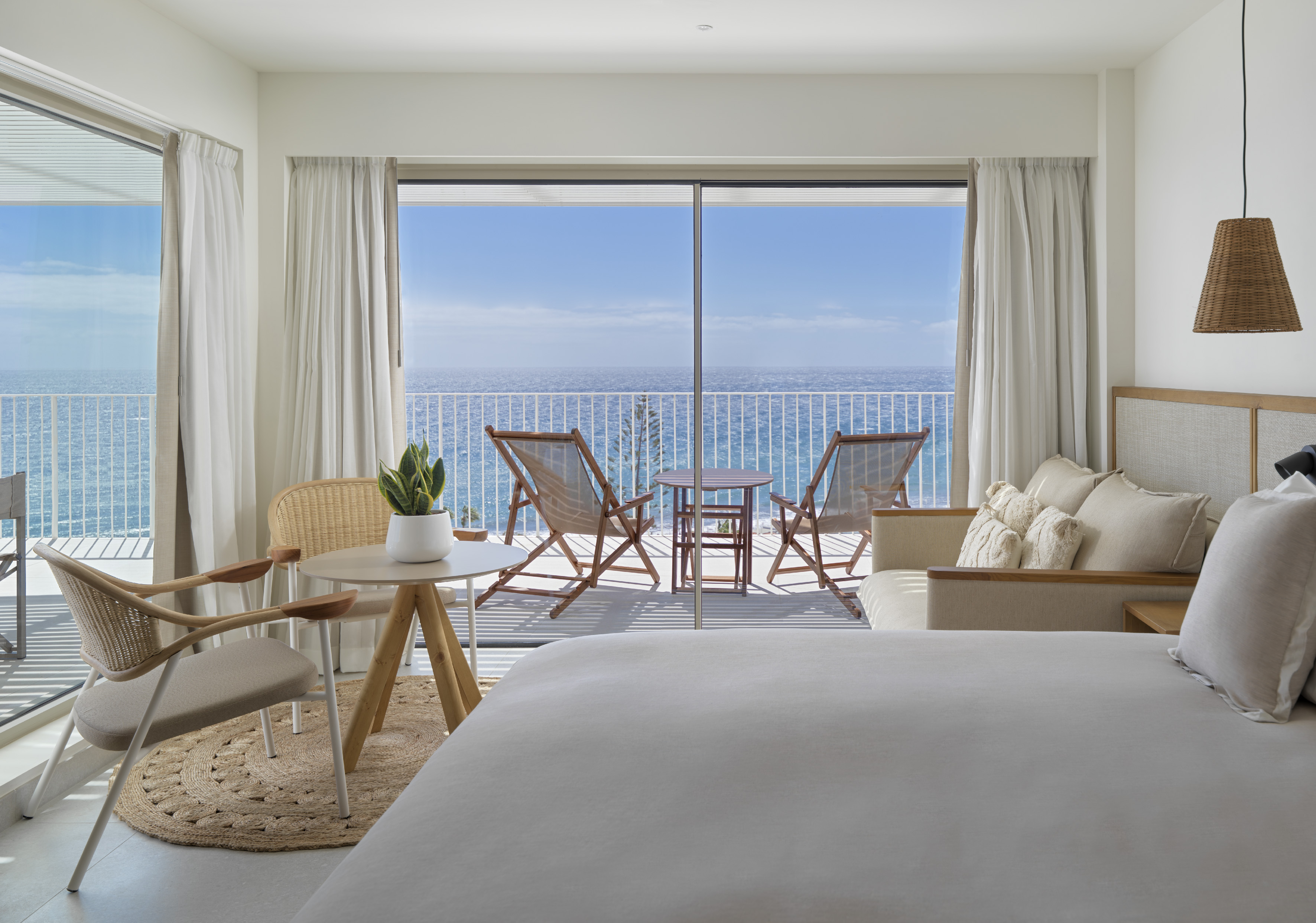 Modern resort room with ocean view balcony and lounge chairs.