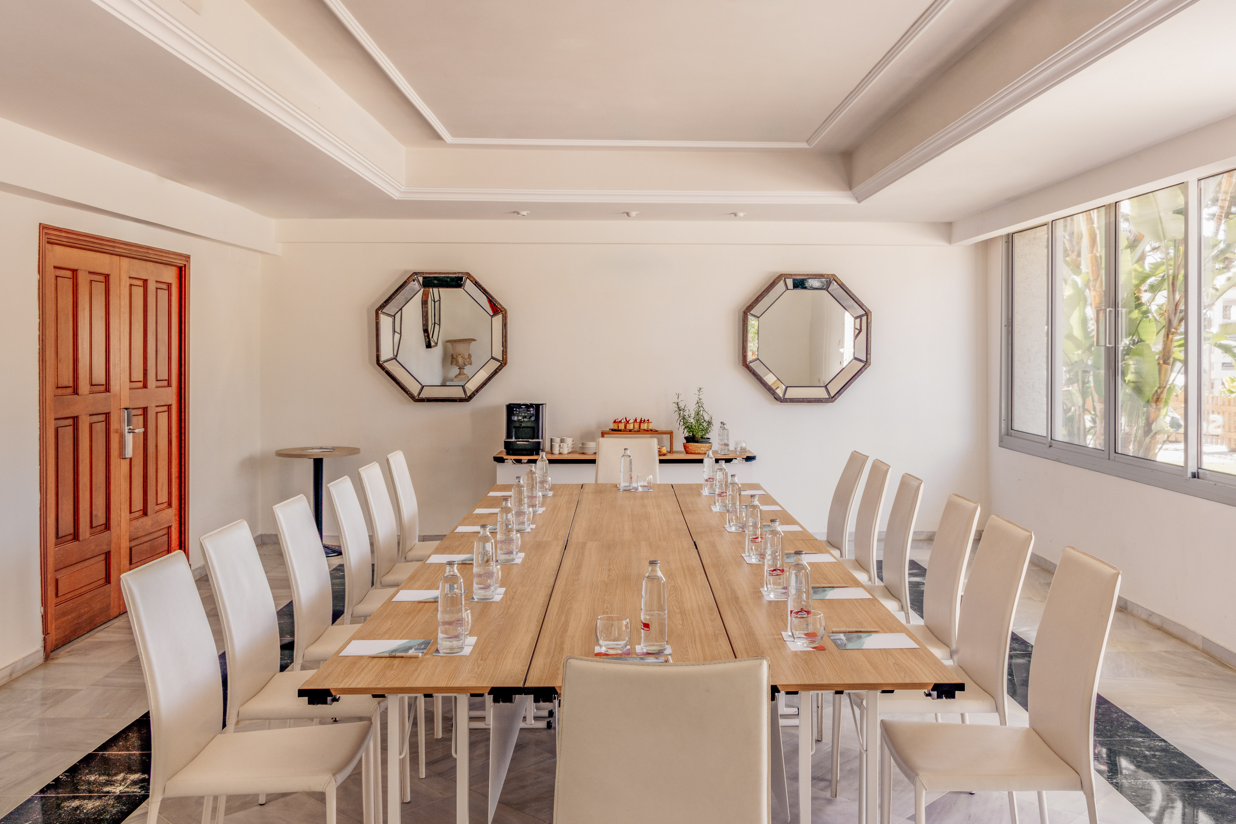 Conference room with long wooden table, white chairs, water, and large windows.