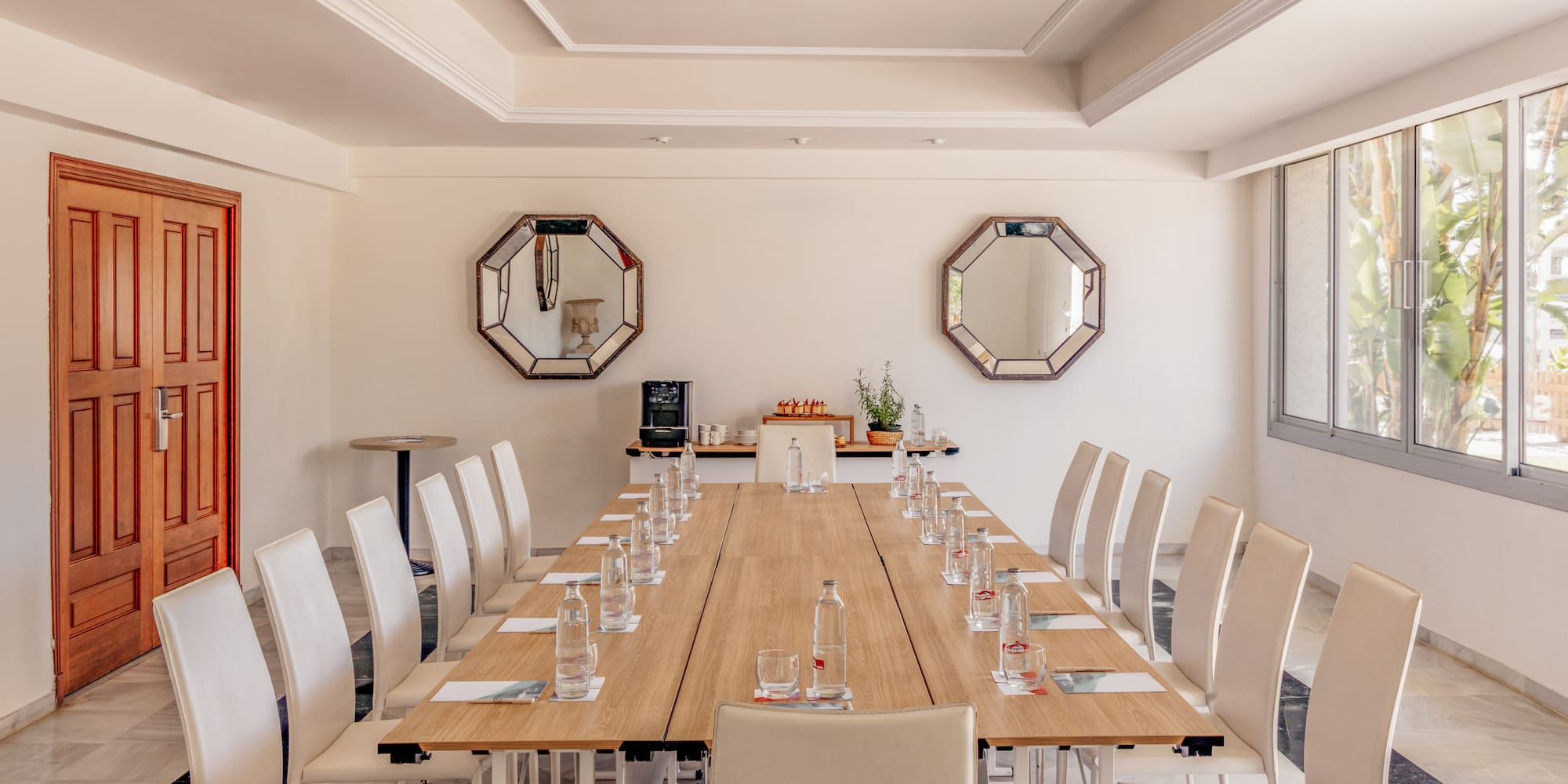 Conference room with long wooden table, white chairs, water, and large windows.