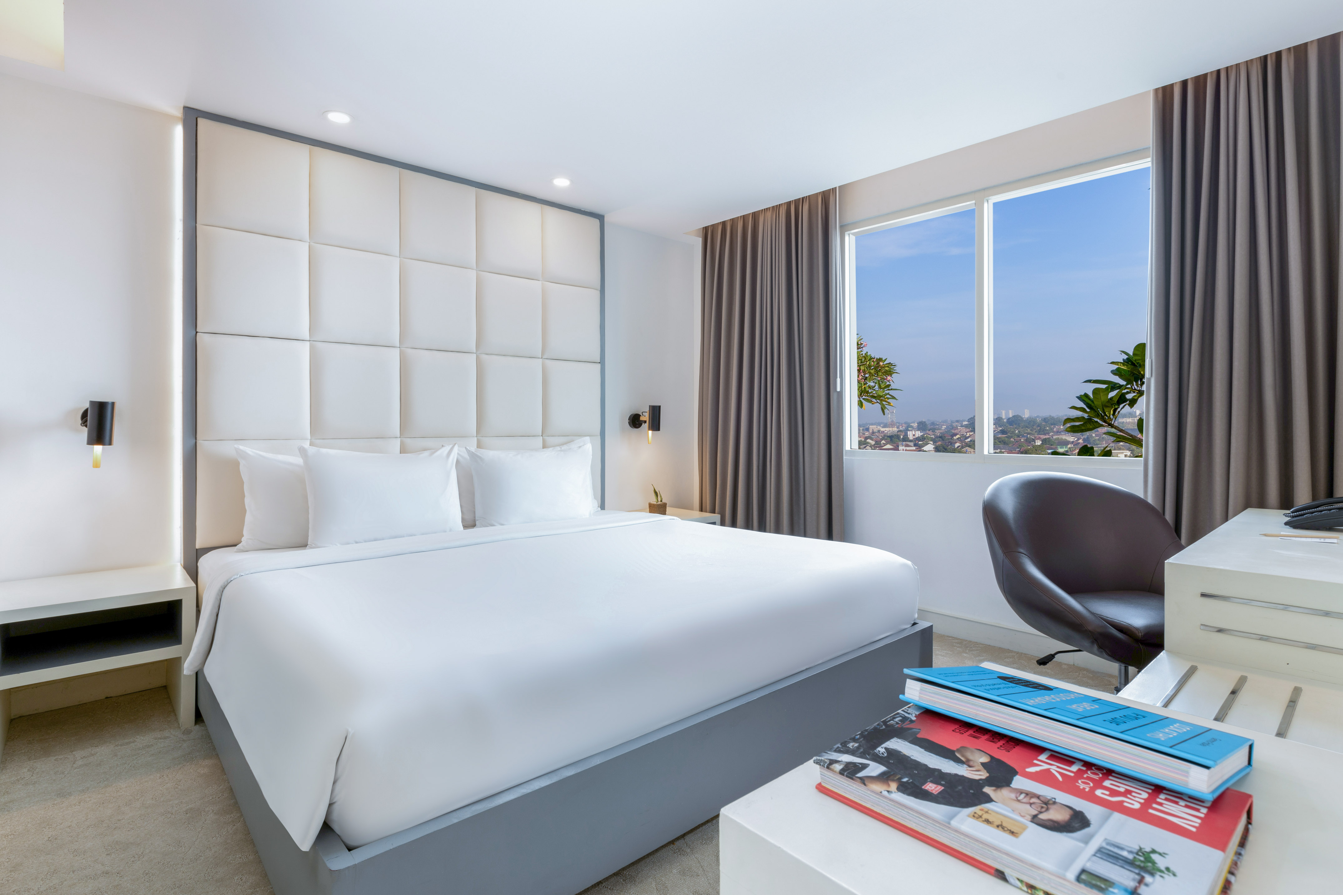 Modern hotel room with king bed, city view window, and work desk.