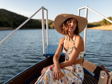 Woman in straw hat and 'Toscana' floral outfit on lake boat.