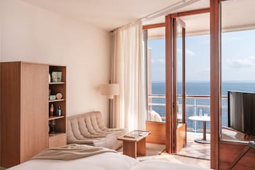 a room with a bed and a couch and a table with a view of the ocean