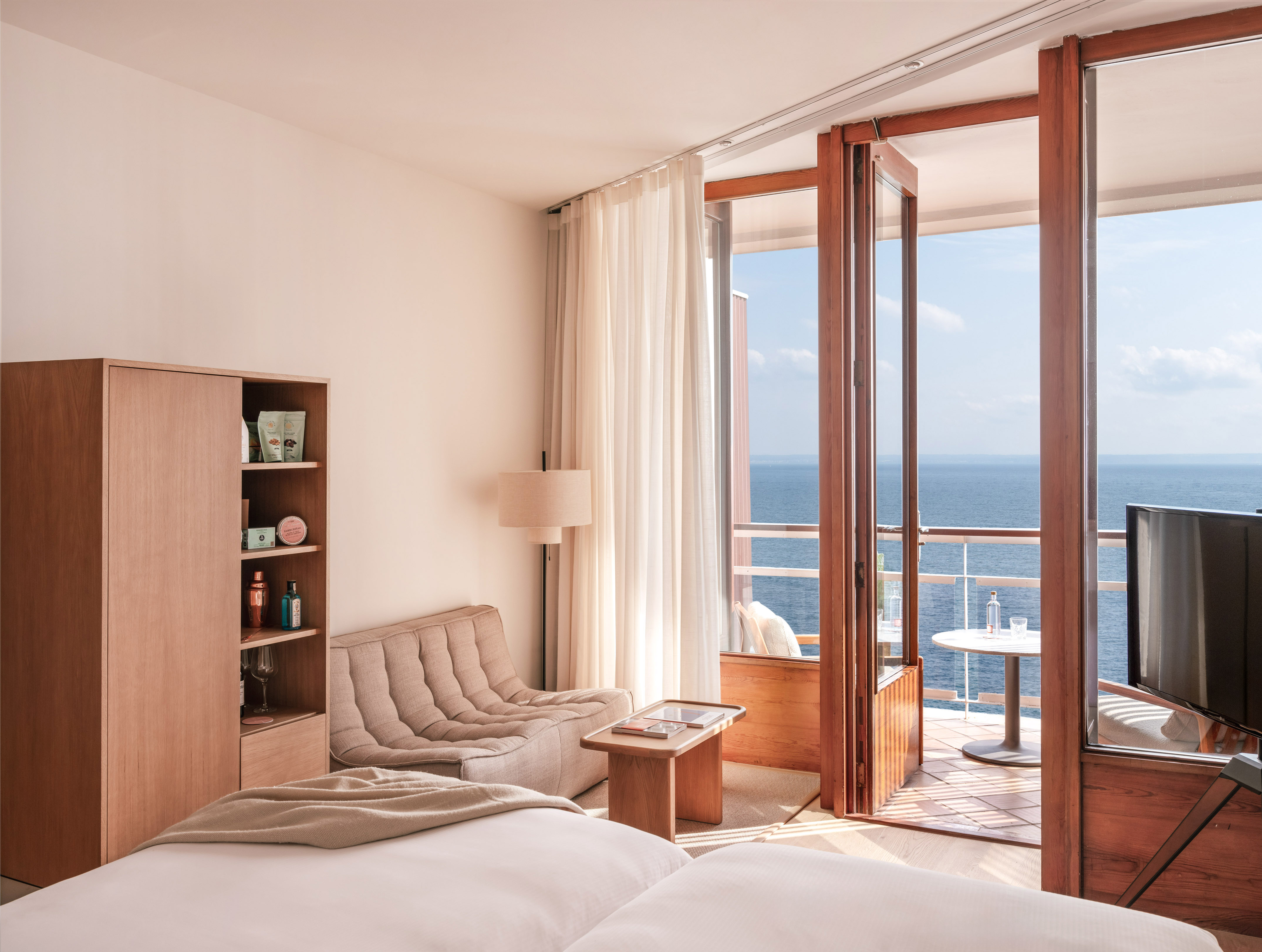 Minimalist hotel room with private ocean-view balcony.