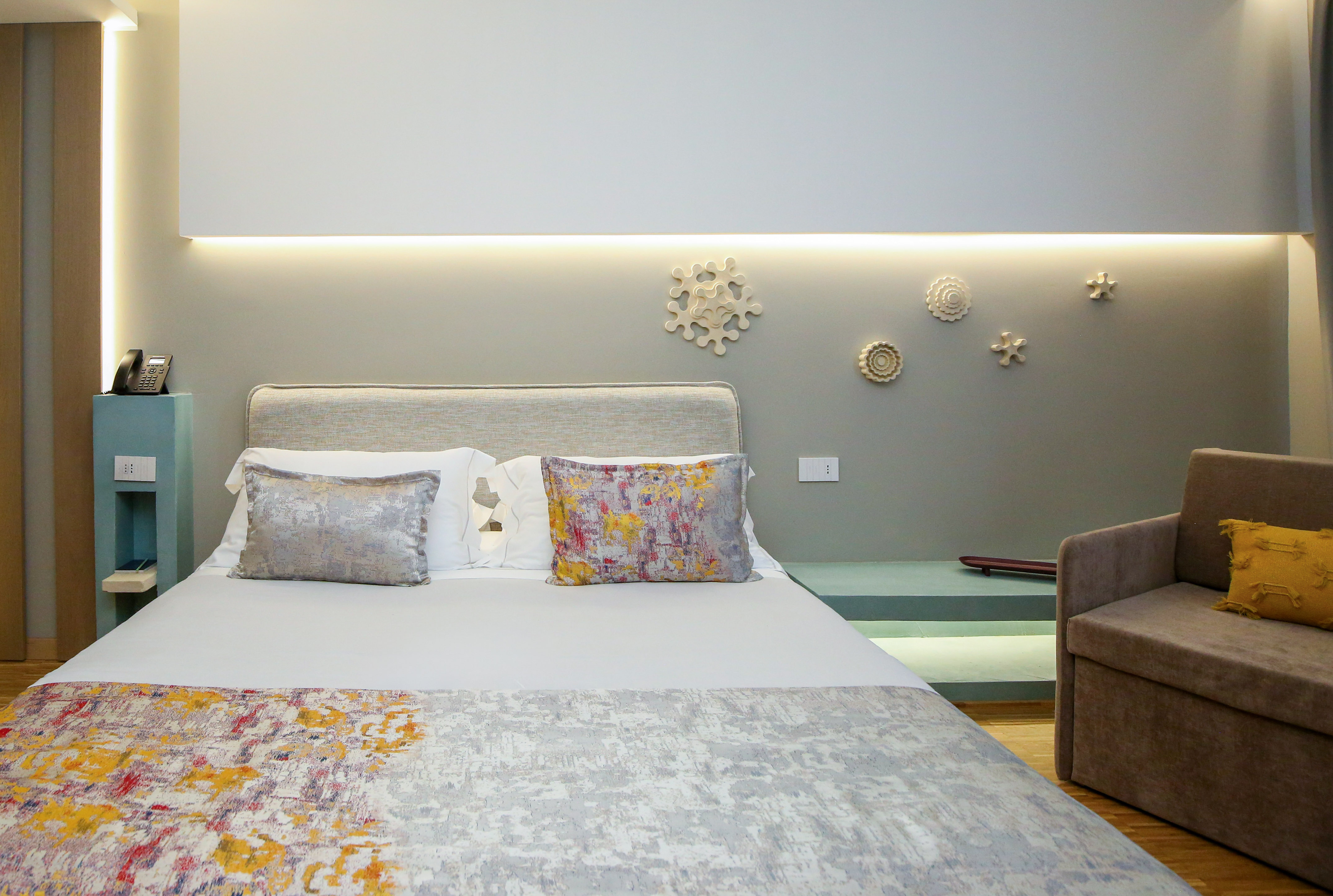 Modern hotel bedroom with colorful bed, grey headboard, and decorative wall art.