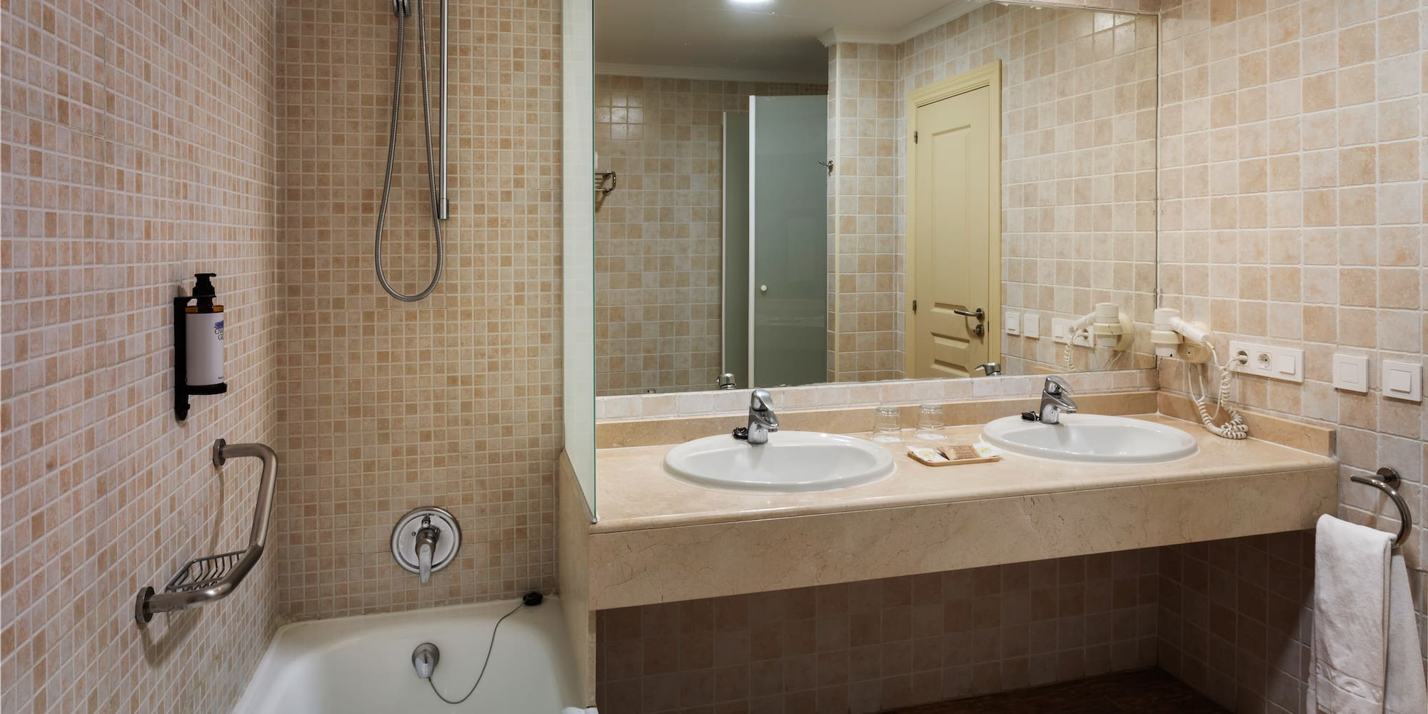 Beige tiled bathroom with bathtub, shower, double vanity, and large mirror.