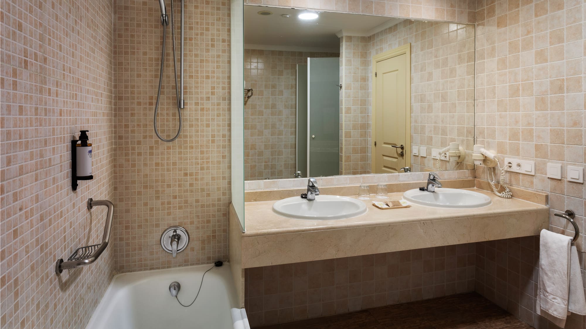 Beige tiled bathroom with bathtub, shower, double vanity, and large mirror.