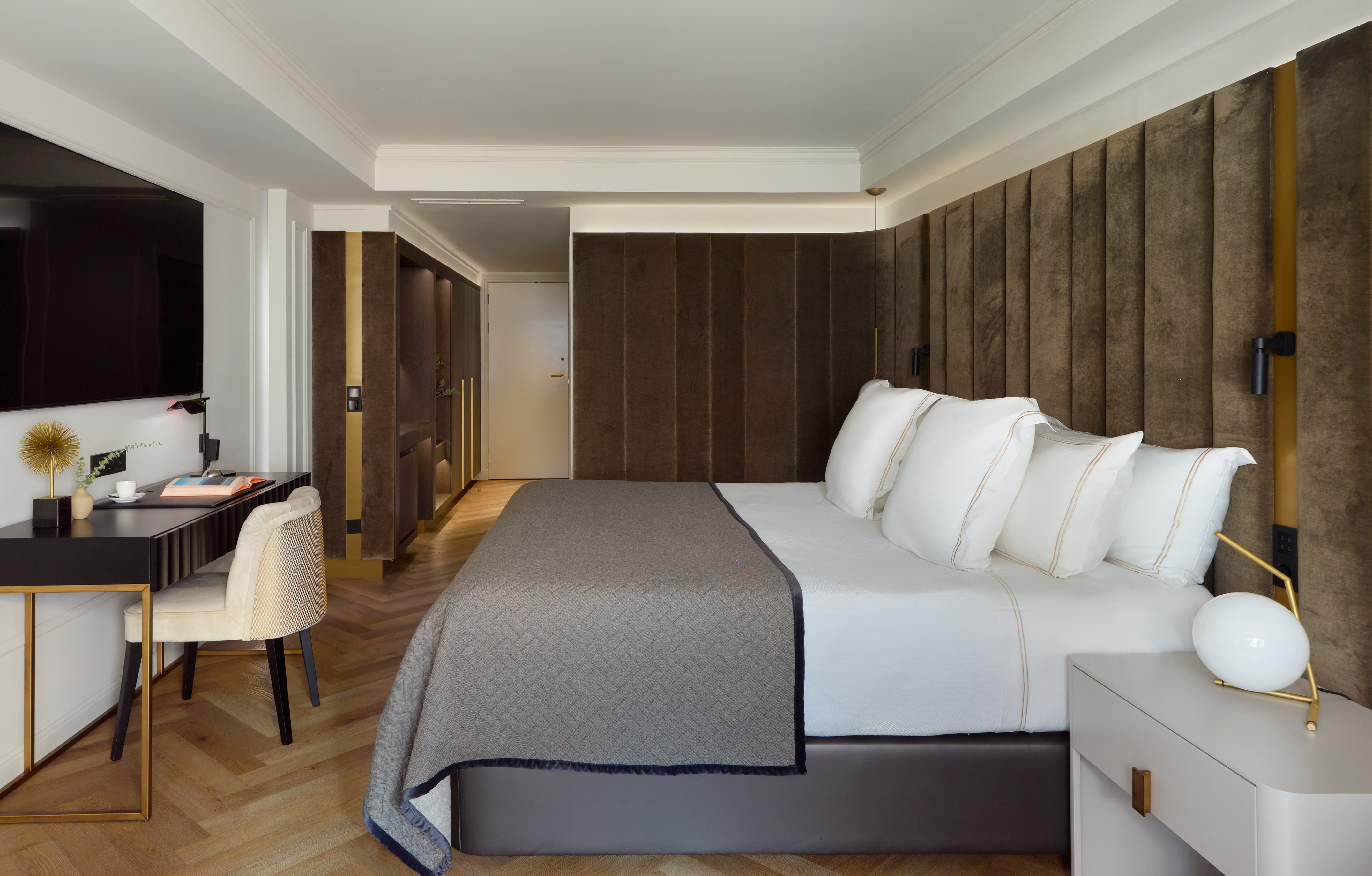 Modern hotel bedroom with large bed, brown padded headboard, and work desk.