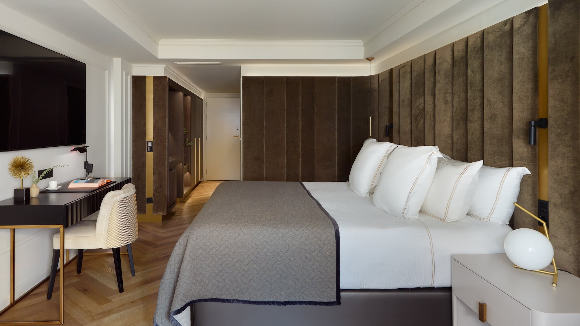 Modern hotel bedroom with large bed, brown padded headboard, and work desk.