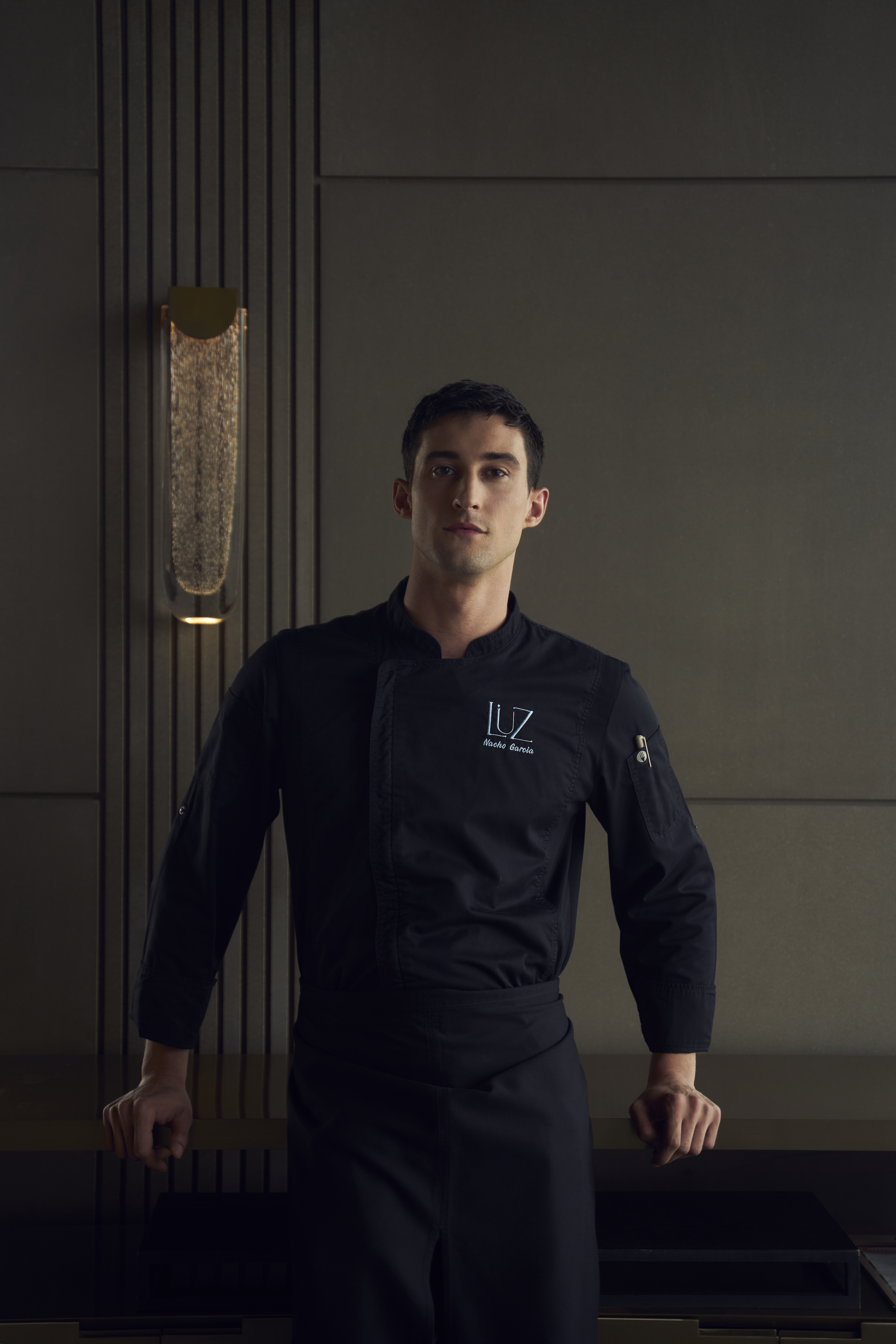 Chef Nacho Garcia in black uniform, standing in a sleek modern restaurant.