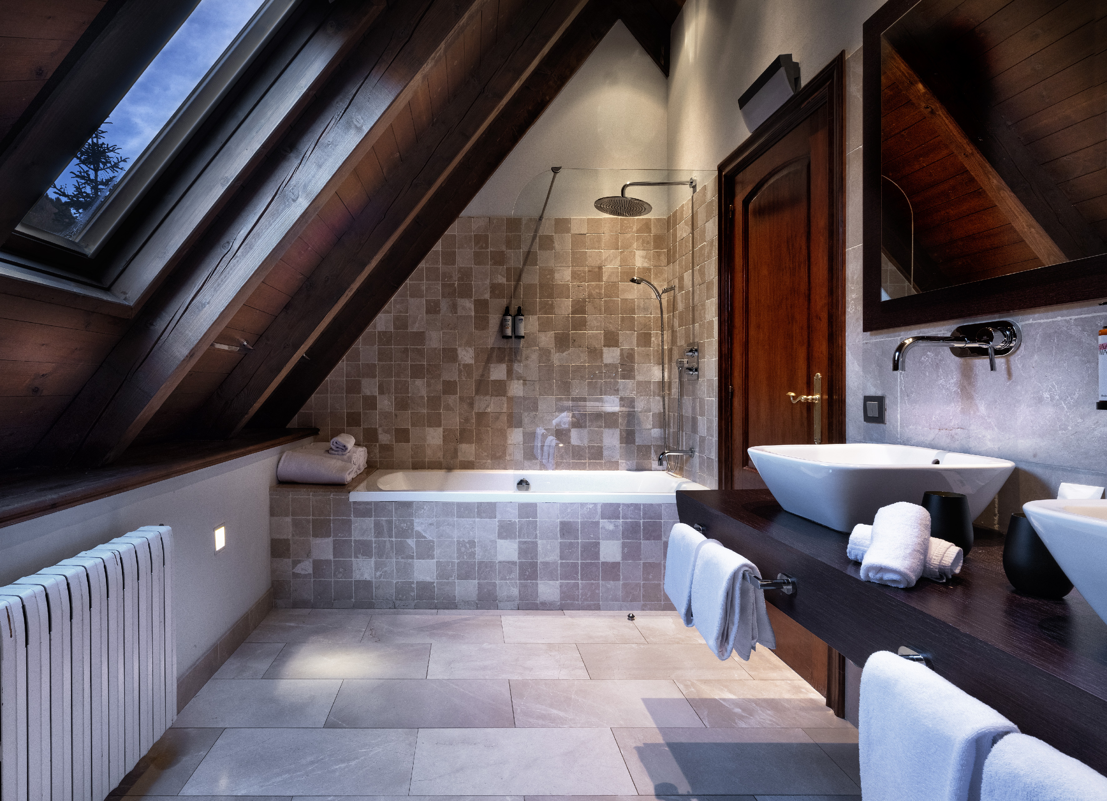 Loft bathroom with skylight, wood beams, tiled shower, tub, and modern vanity.
