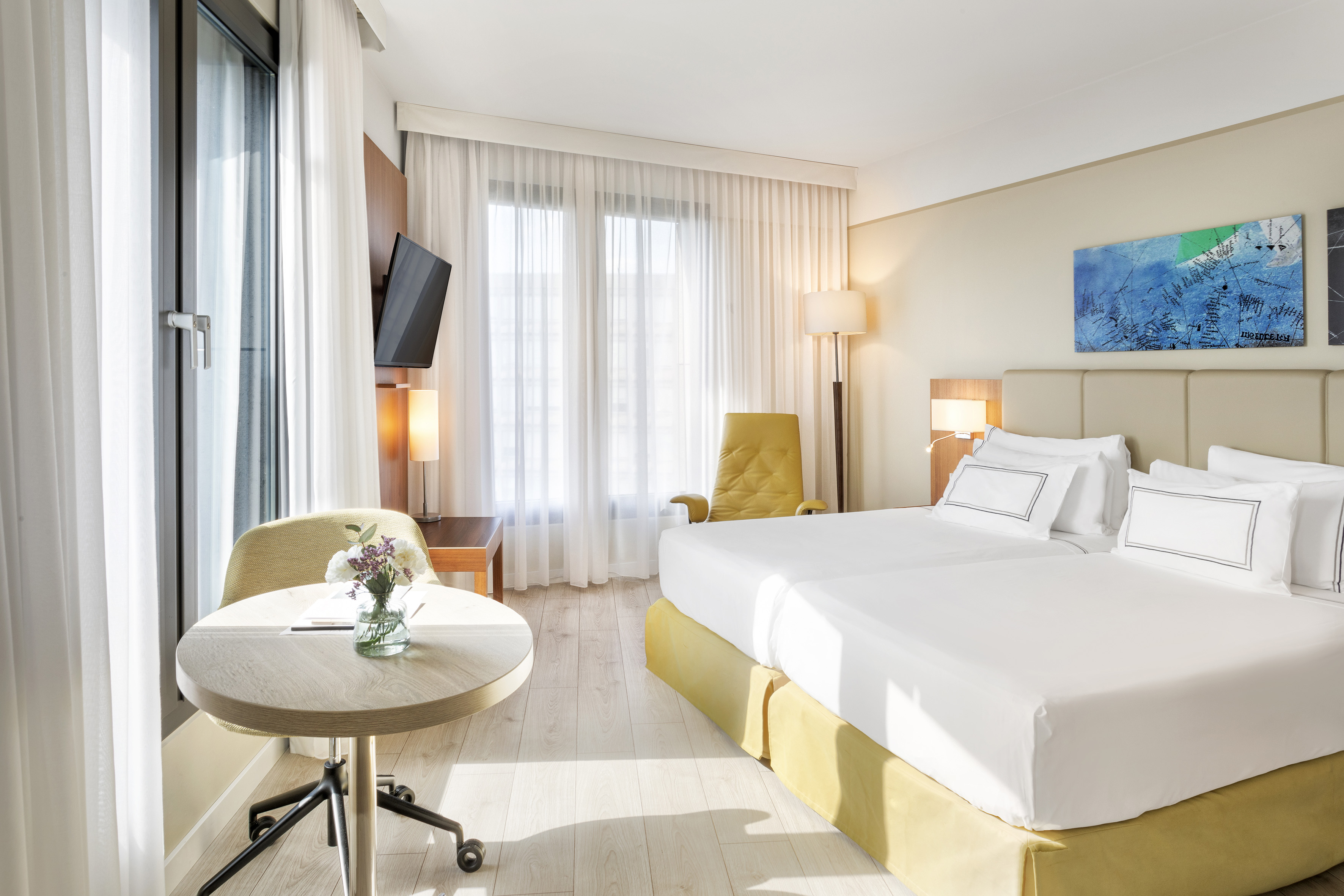 Hotel room with twin beds, bright window, modern decor, and wood floor.