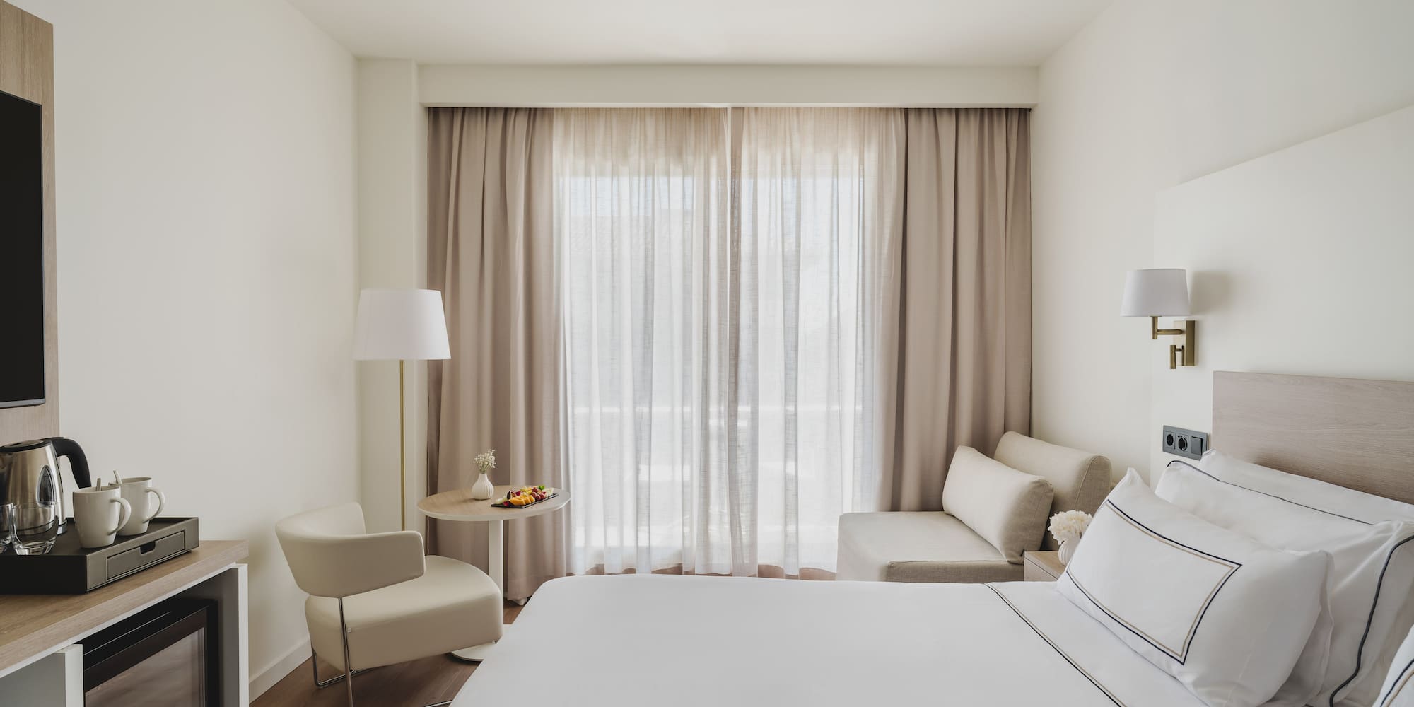 Luminosa habitación de hotel moderna con cama, zona de estar y minibar.
