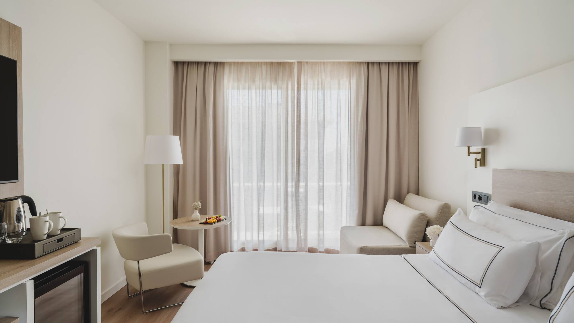 Luminosa habitación de hotel moderna con cama, zona de estar y minibar.