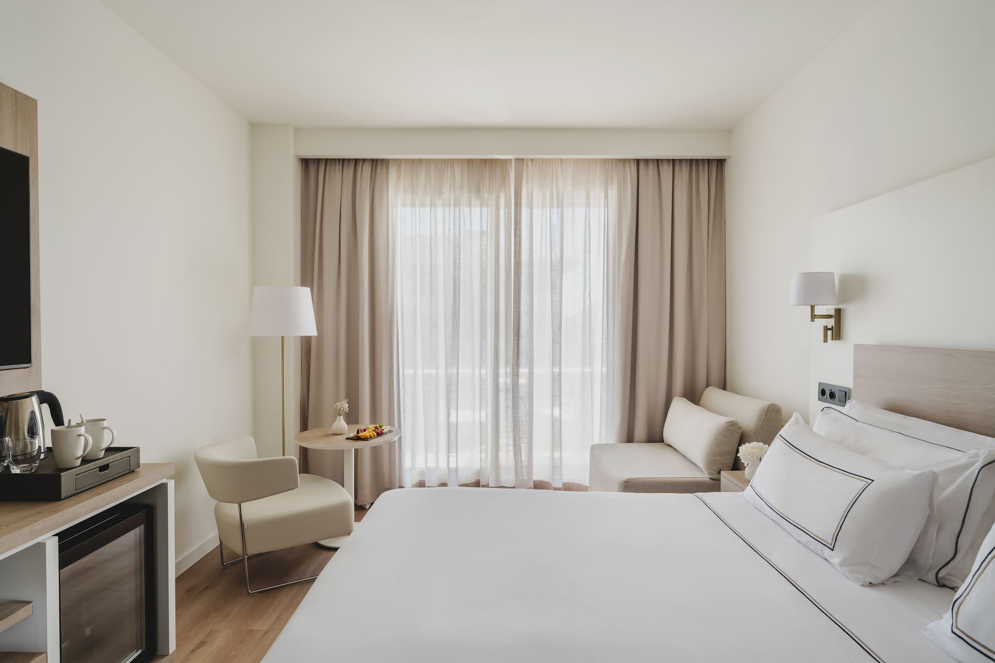 Luminosa habitación de hotel moderna con cama, zona de estar y minibar.