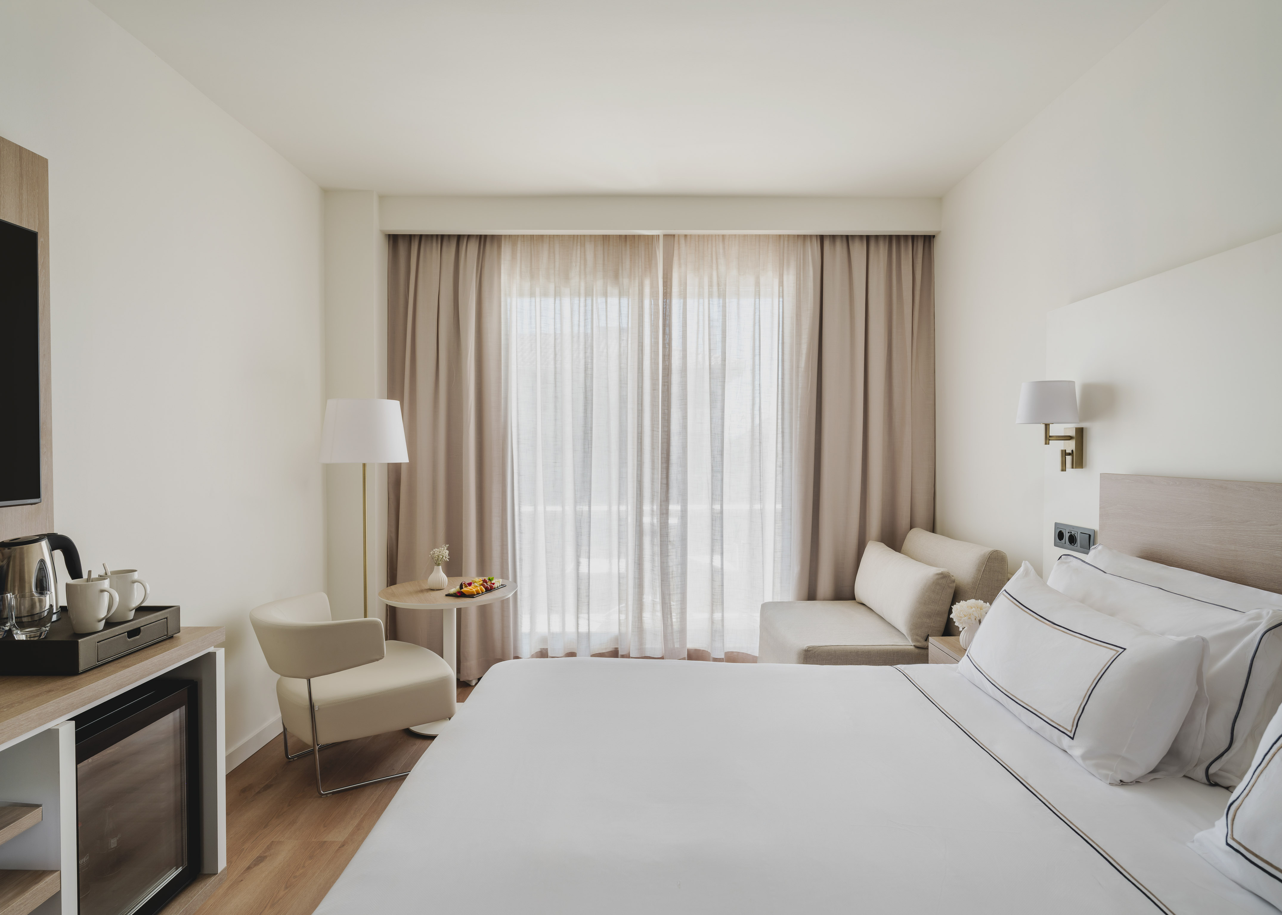 Luminosa habitación de hotel moderna con cama, zona de estar y minibar.