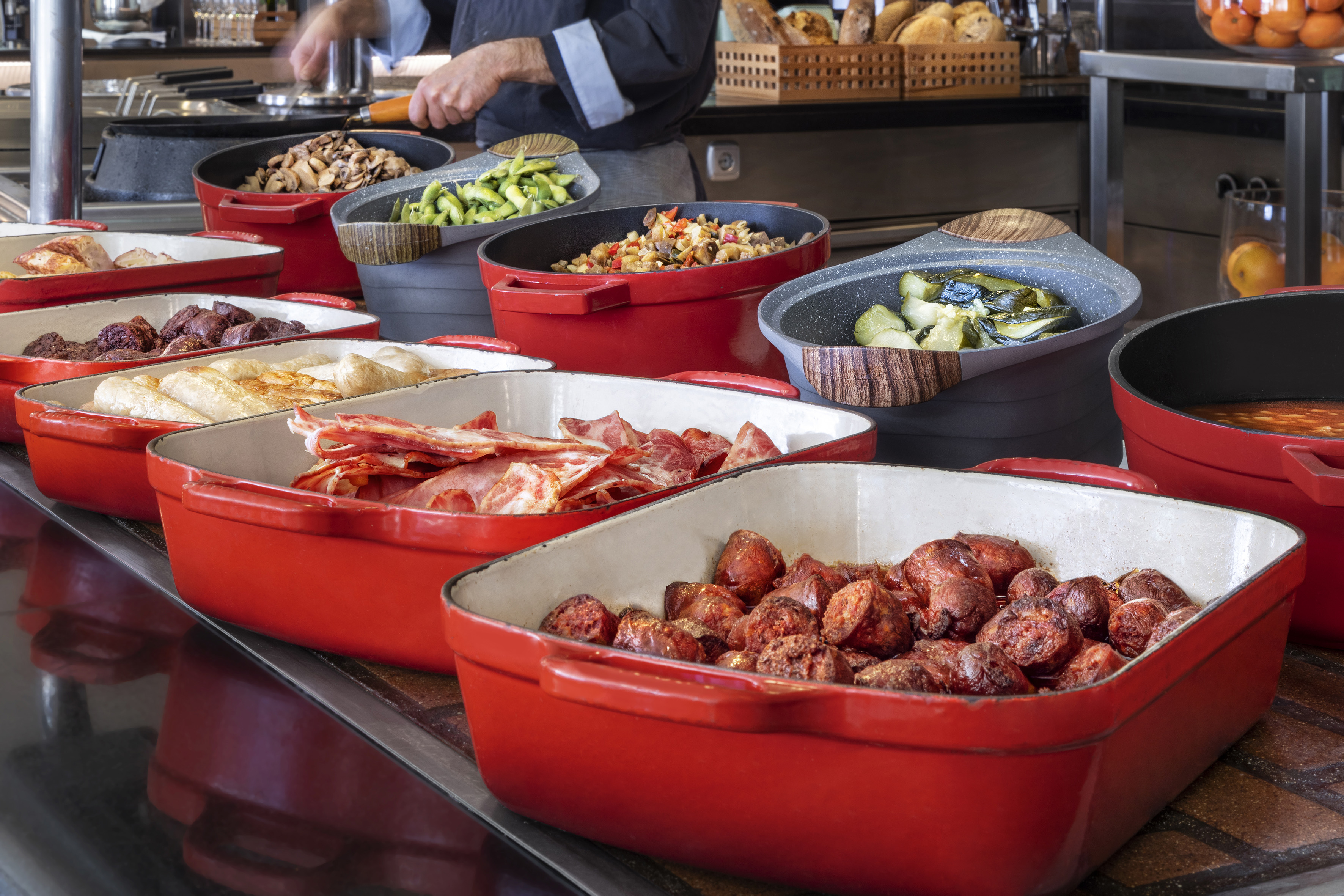 Hot breakfast buffet with bacon, sausages, mushrooms, and vegetables.