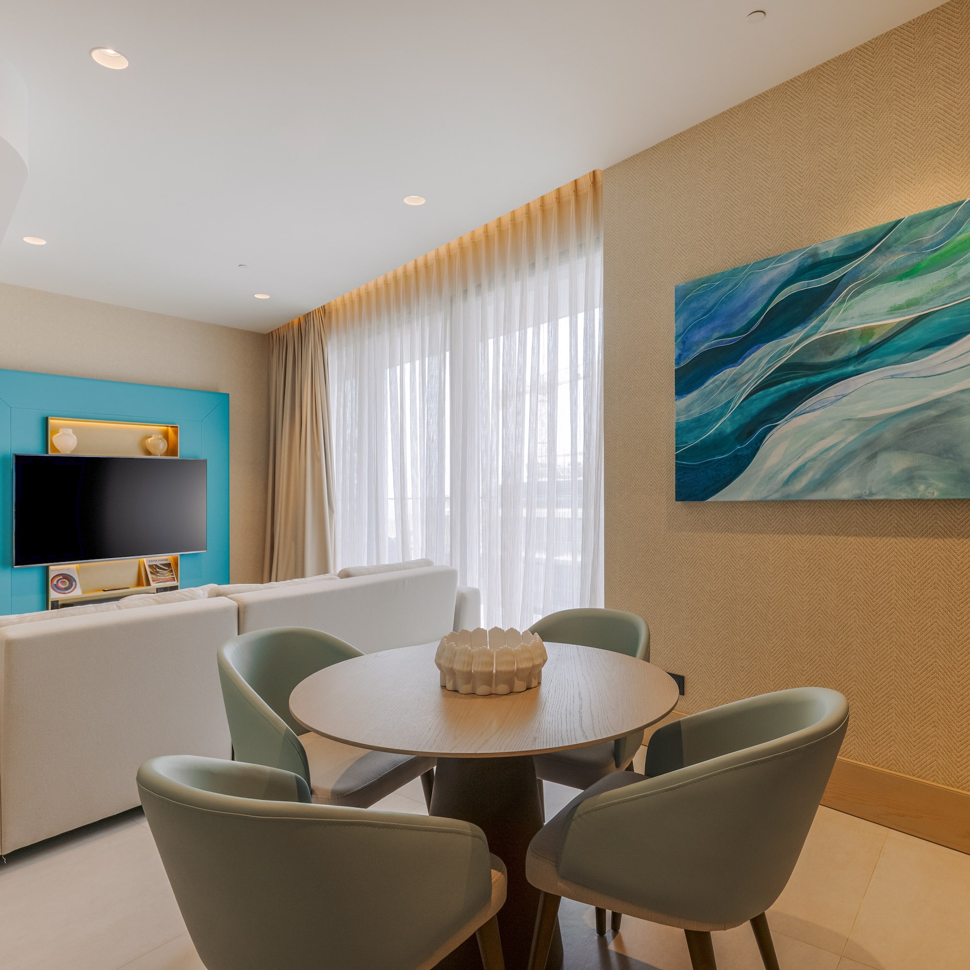 Modern living room: white sofa, round dining table, TV, blue abstract painting.