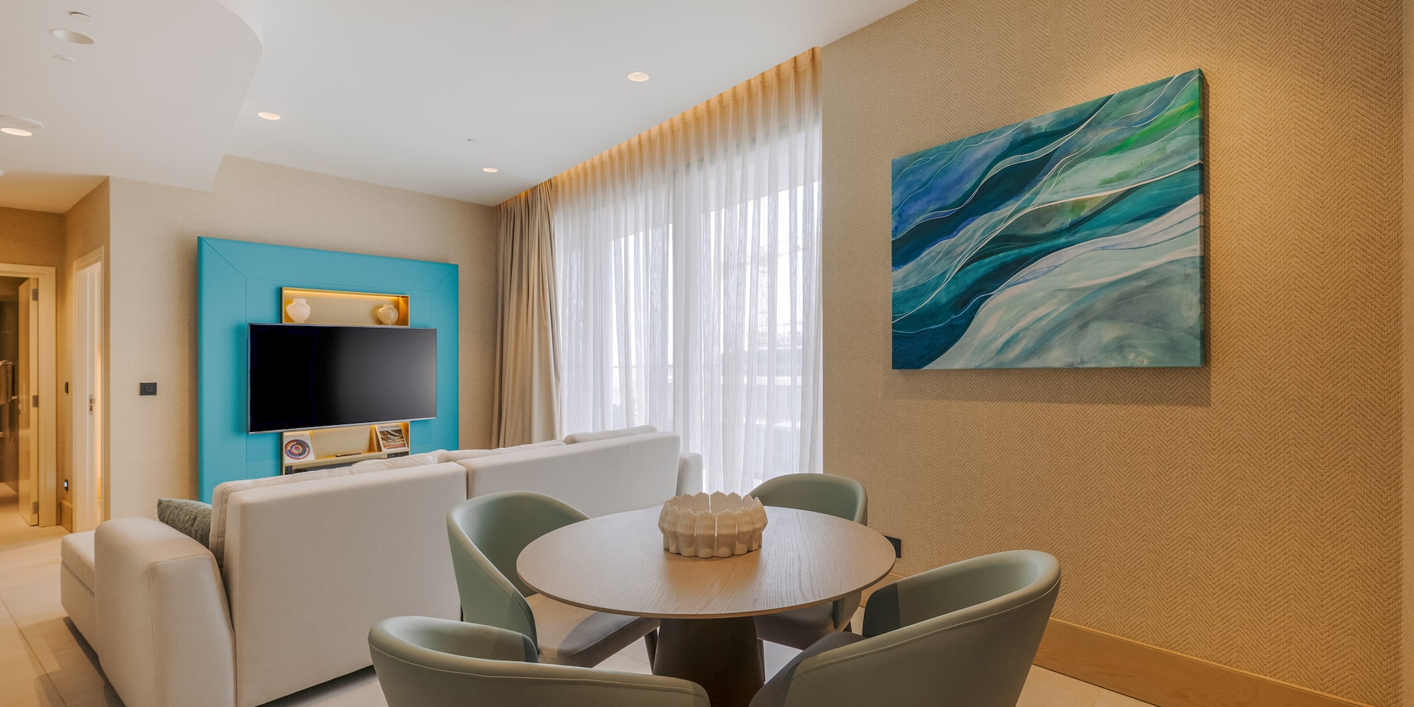 Modern living room: white sofa, round dining table, TV, blue abstract painting.