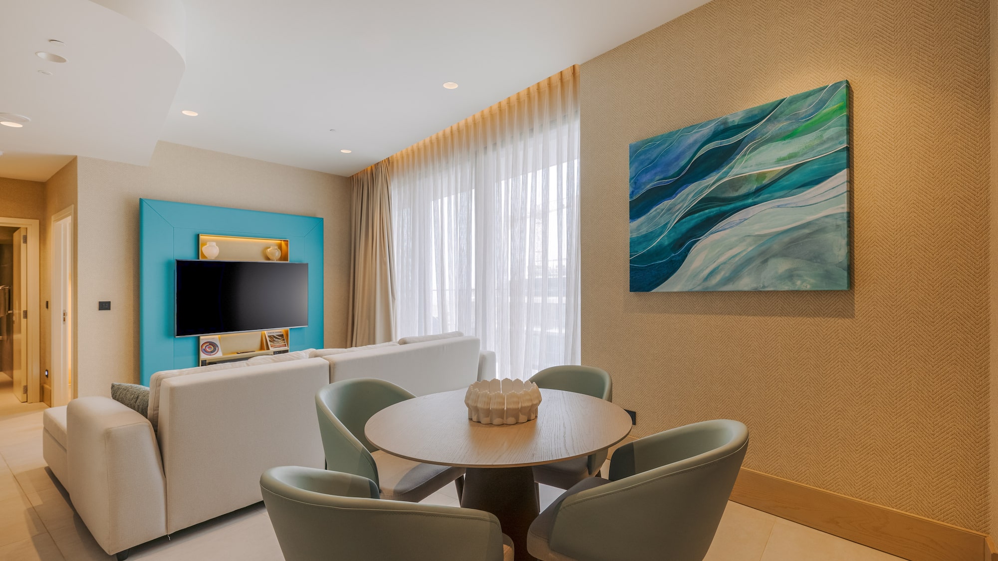 Modern living room: white sofa, round dining table, TV, blue abstract painting.