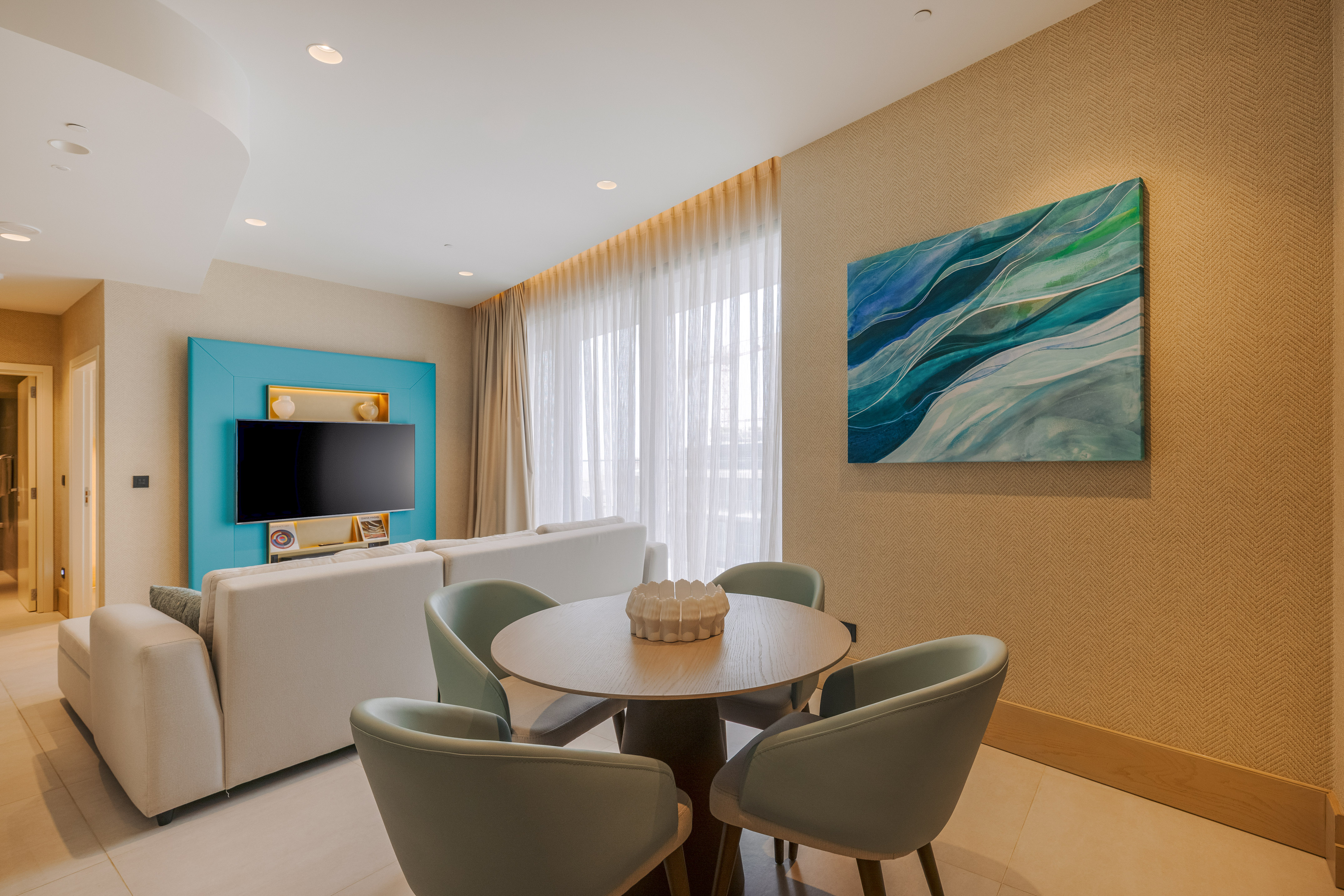 Modern living room: white sofa, round dining table, TV, blue abstract painting.