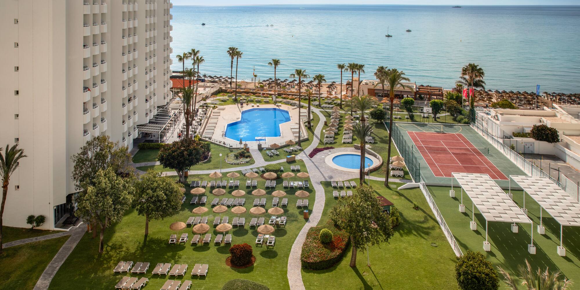 Beachfront hotel with swimming pools, tennis court, palm trees, and ocean.
