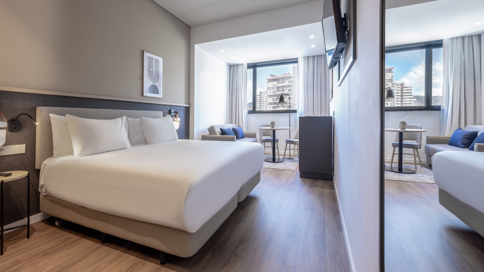 Contemporary hotel suite with king bed, city view, and lounge area.