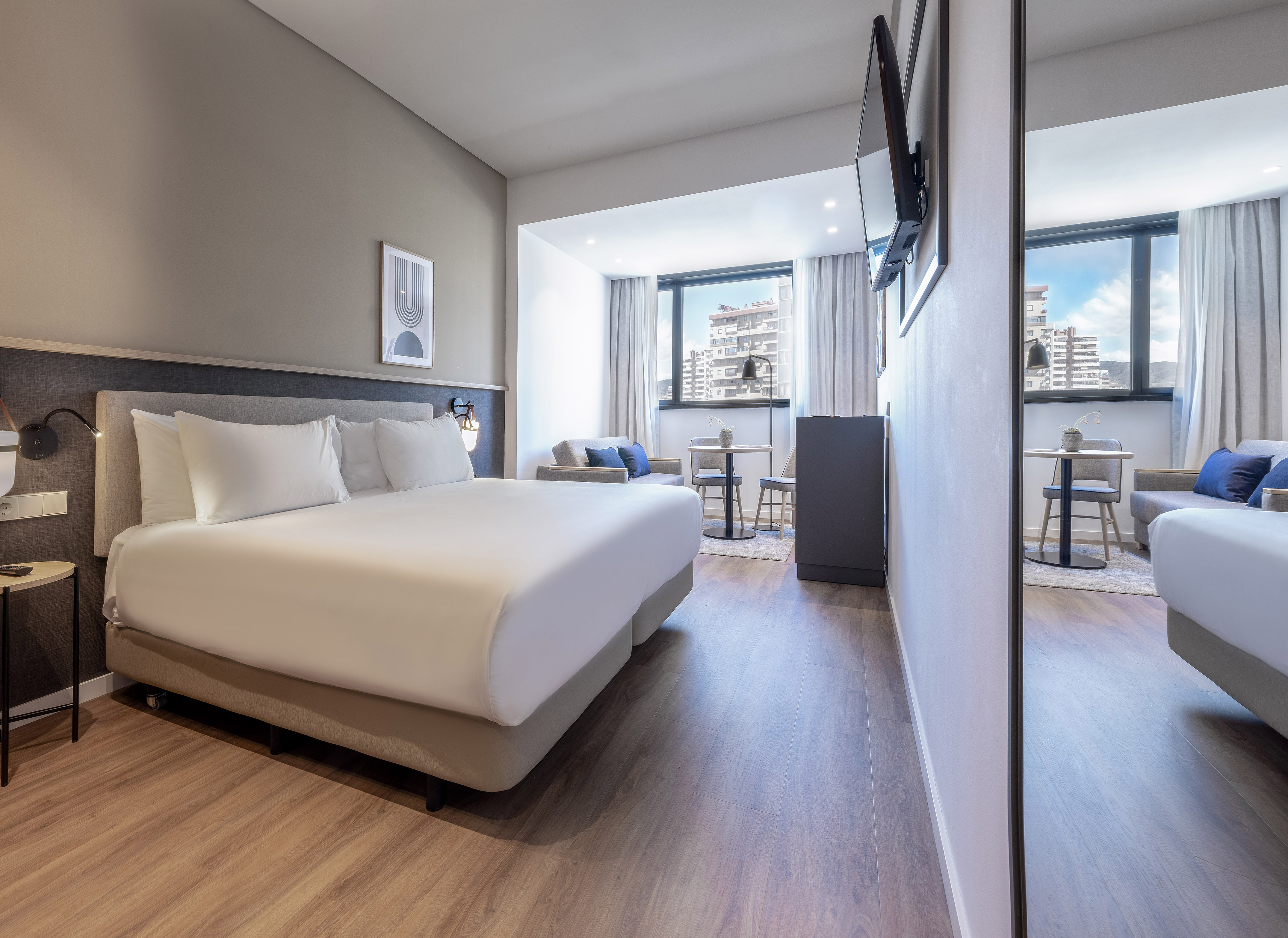 Contemporary hotel suite with king bed, city view, and lounge area.
