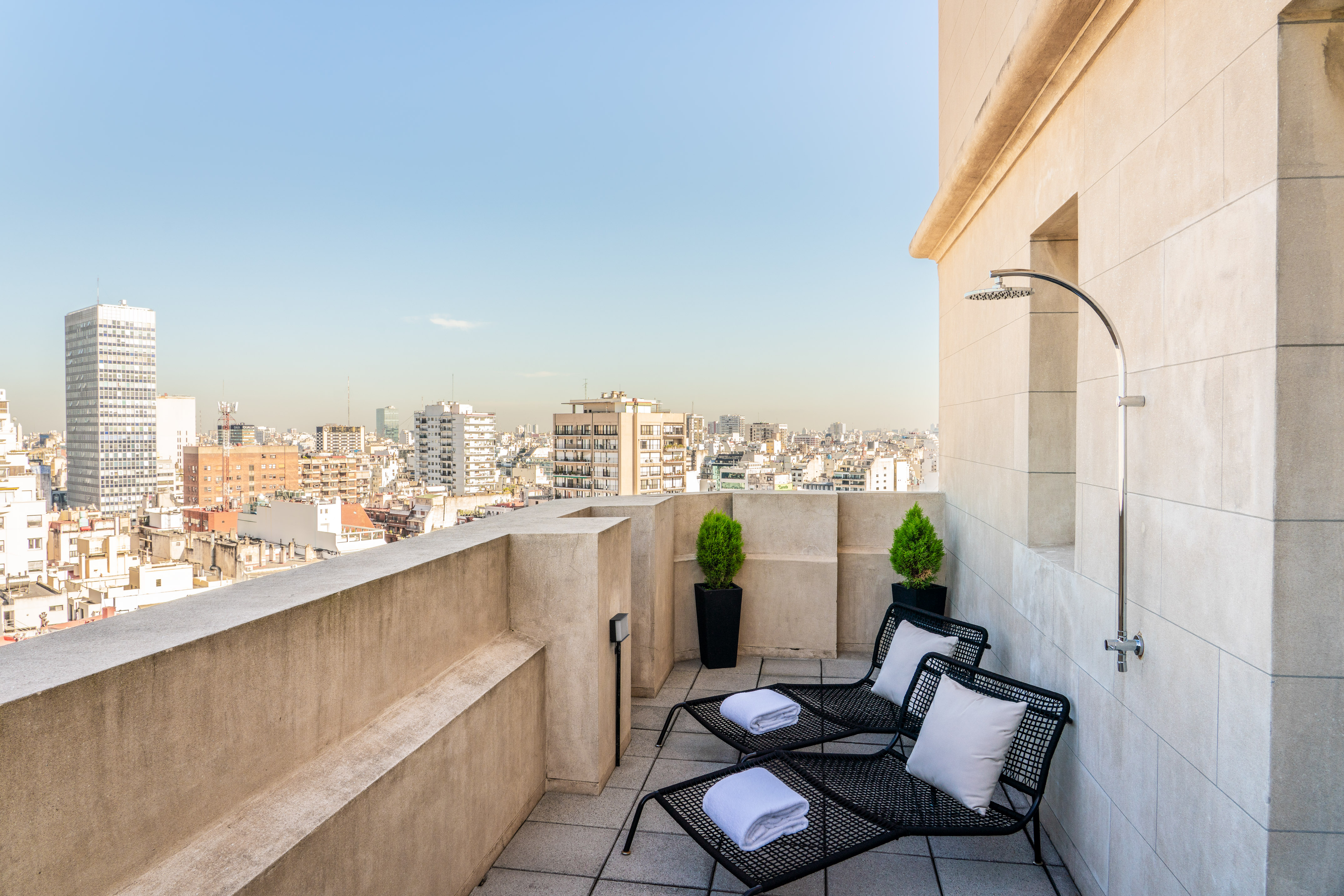 Rooftop terrace with city view, two lounge chairs, and outdoor shower.
